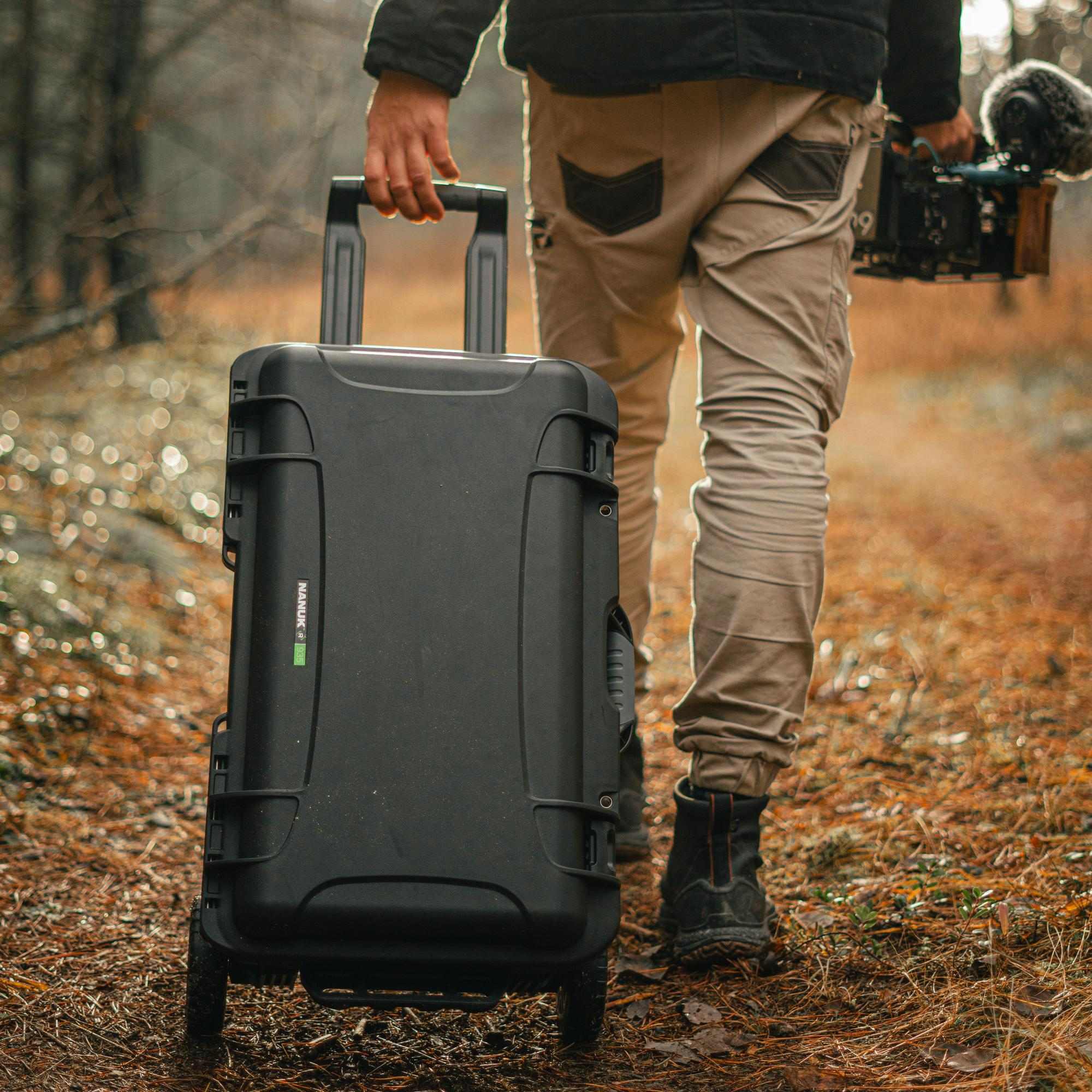 Person walking through a forest with a large black suitcase.