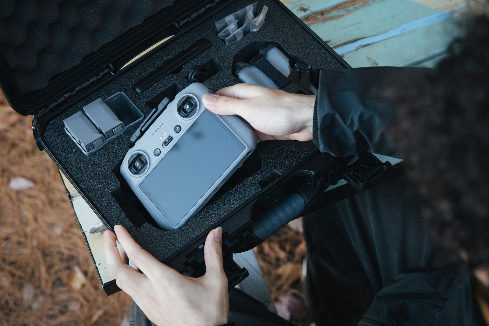 Person holding a drone in a black foam case on a wooden surface