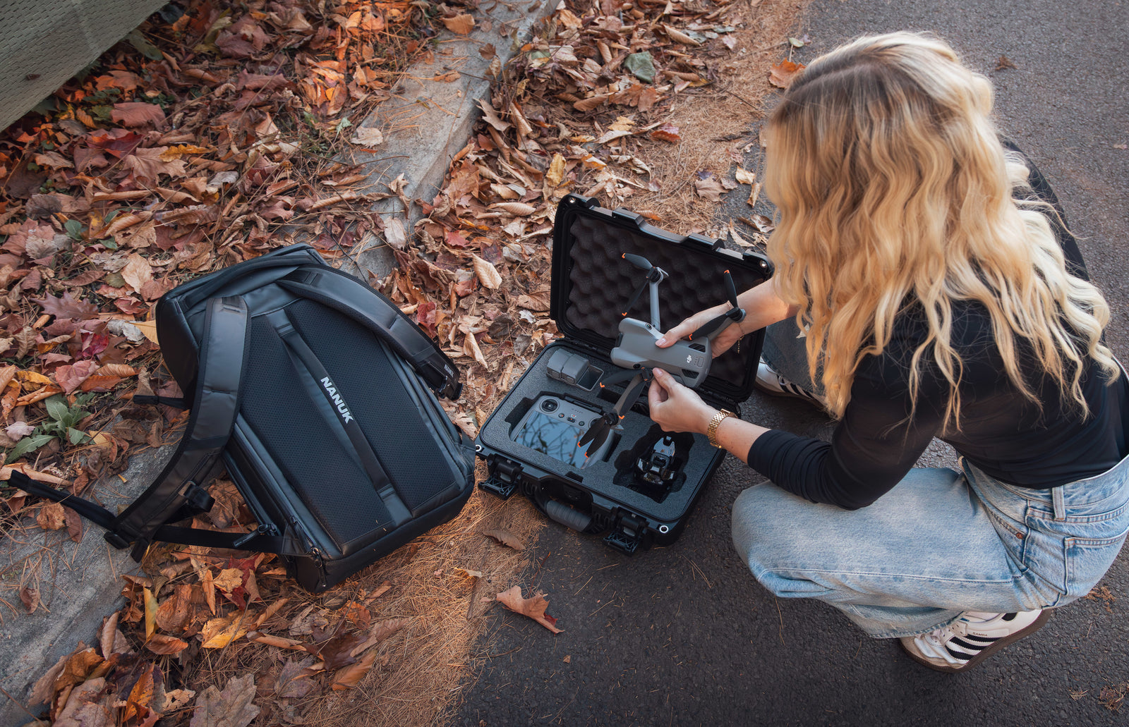 Person unpacking a suitcase on a sidewalk with leaves