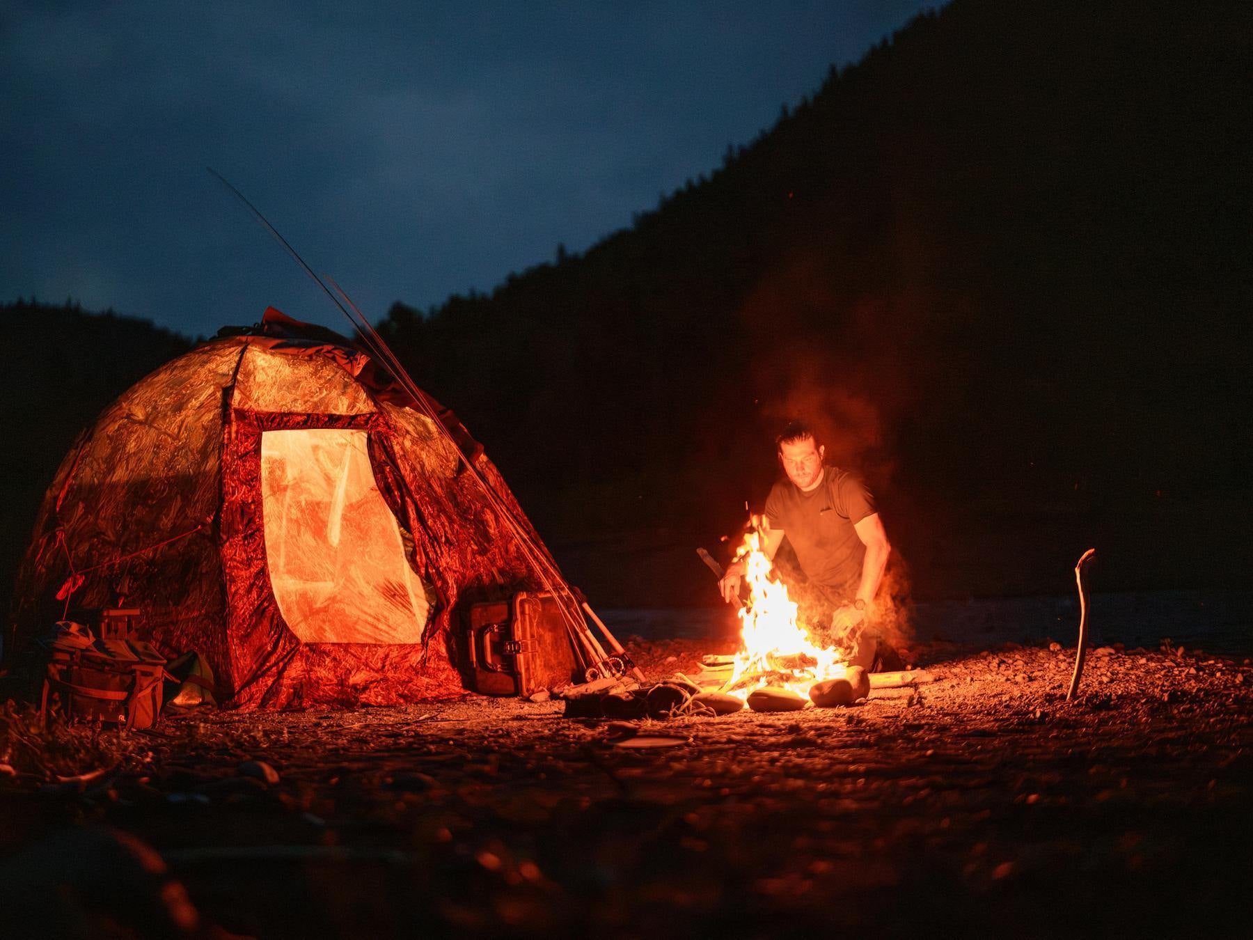 Camping scene with a tent and person by a campfire at night.