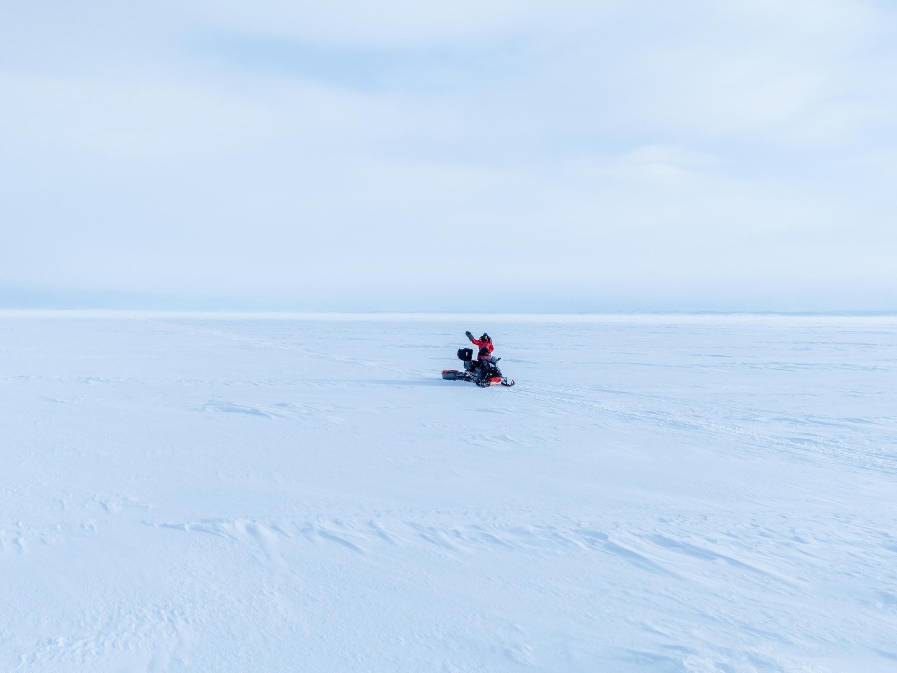 Person on a snowmobile in a vast snowy landscape with a clear blue sky.