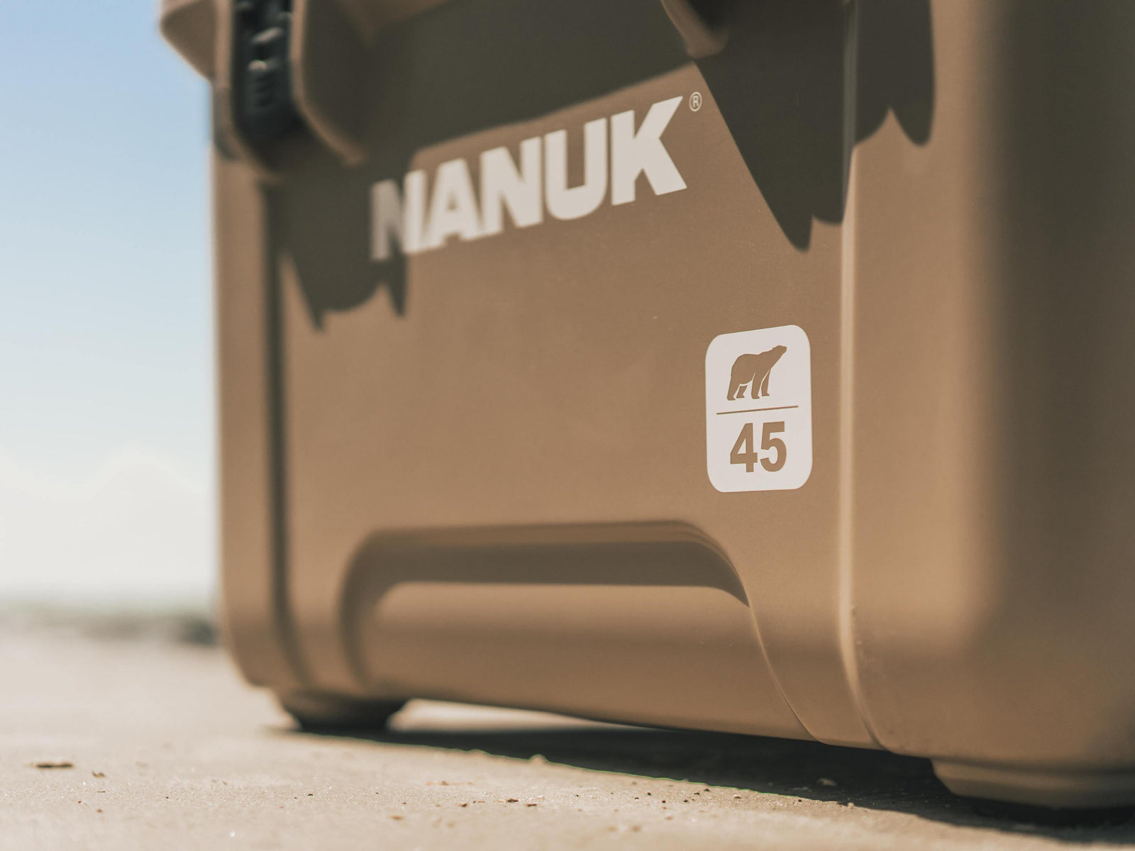 Close-up of a tan Nanuk cooler outdoors, showing the NANUK logo and a white square sticker with a polar bear icon and the number 45.