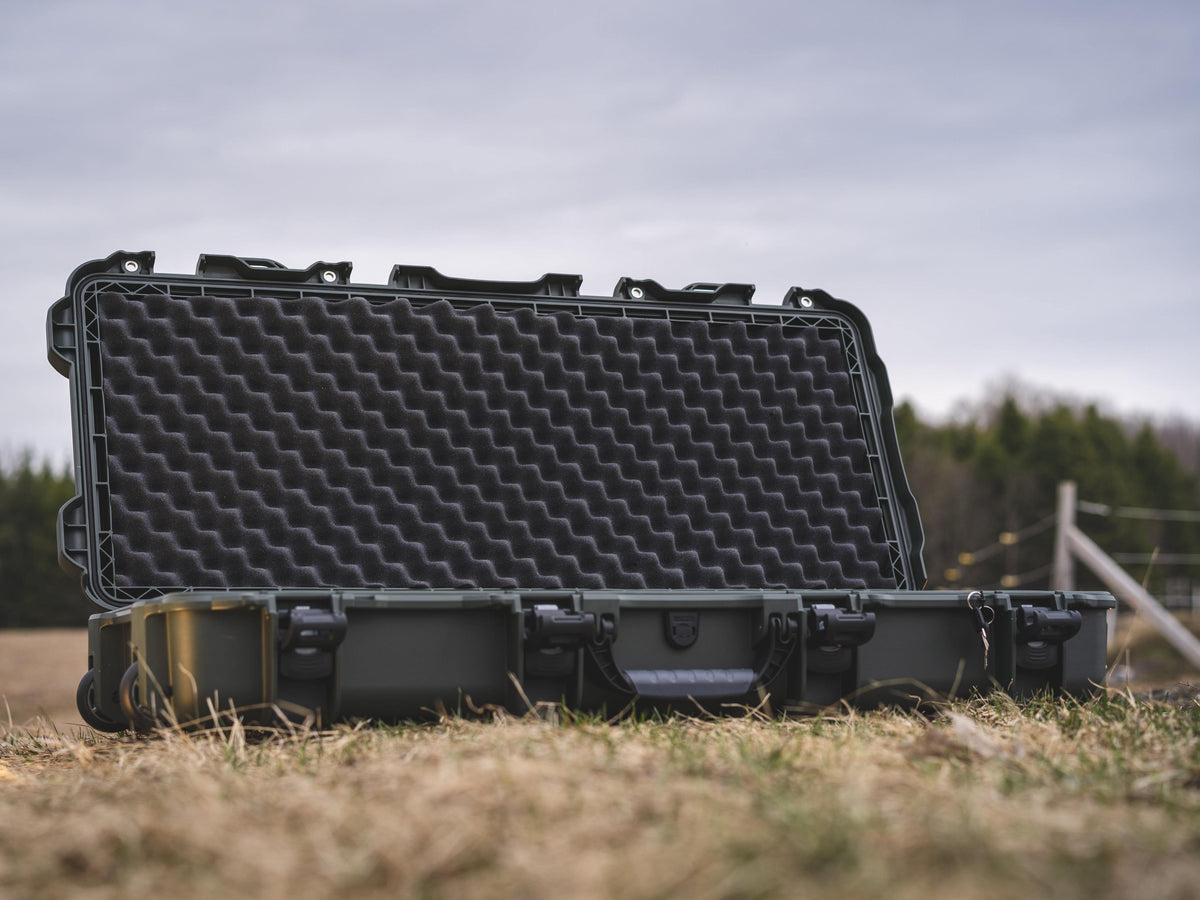 An open heavy-duty protective hard case with a black textured foam insert inside, set outdoors on dry grass with a blurred natural background.