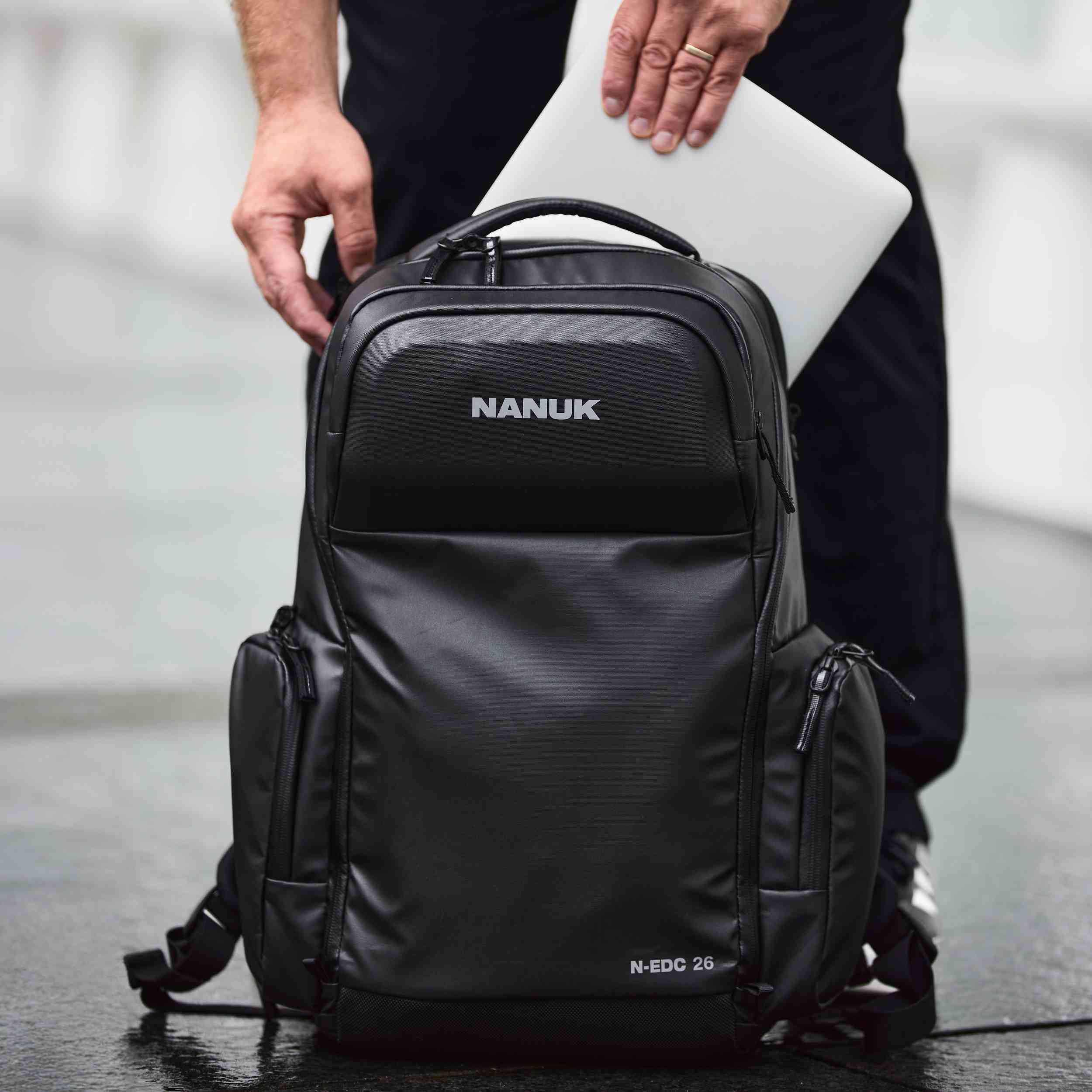 Black Nanuk backpack with a person holding a laptop inside, on a blurred background. Black Nanuk backpack with a person holding a laptop inside, on a blurred background.