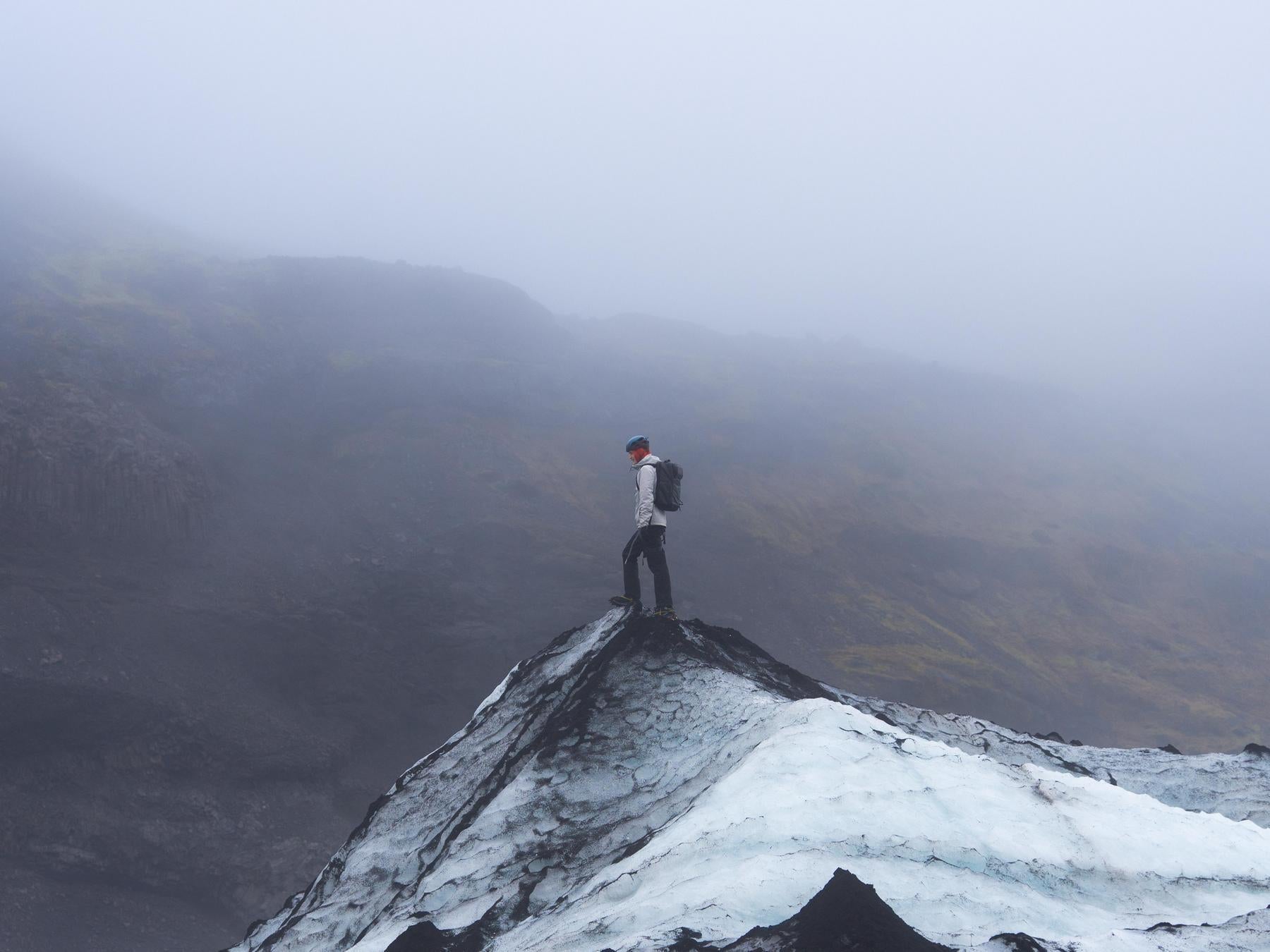 Person standing on a mountain peak with a backpack, surrounded by foggy landscape