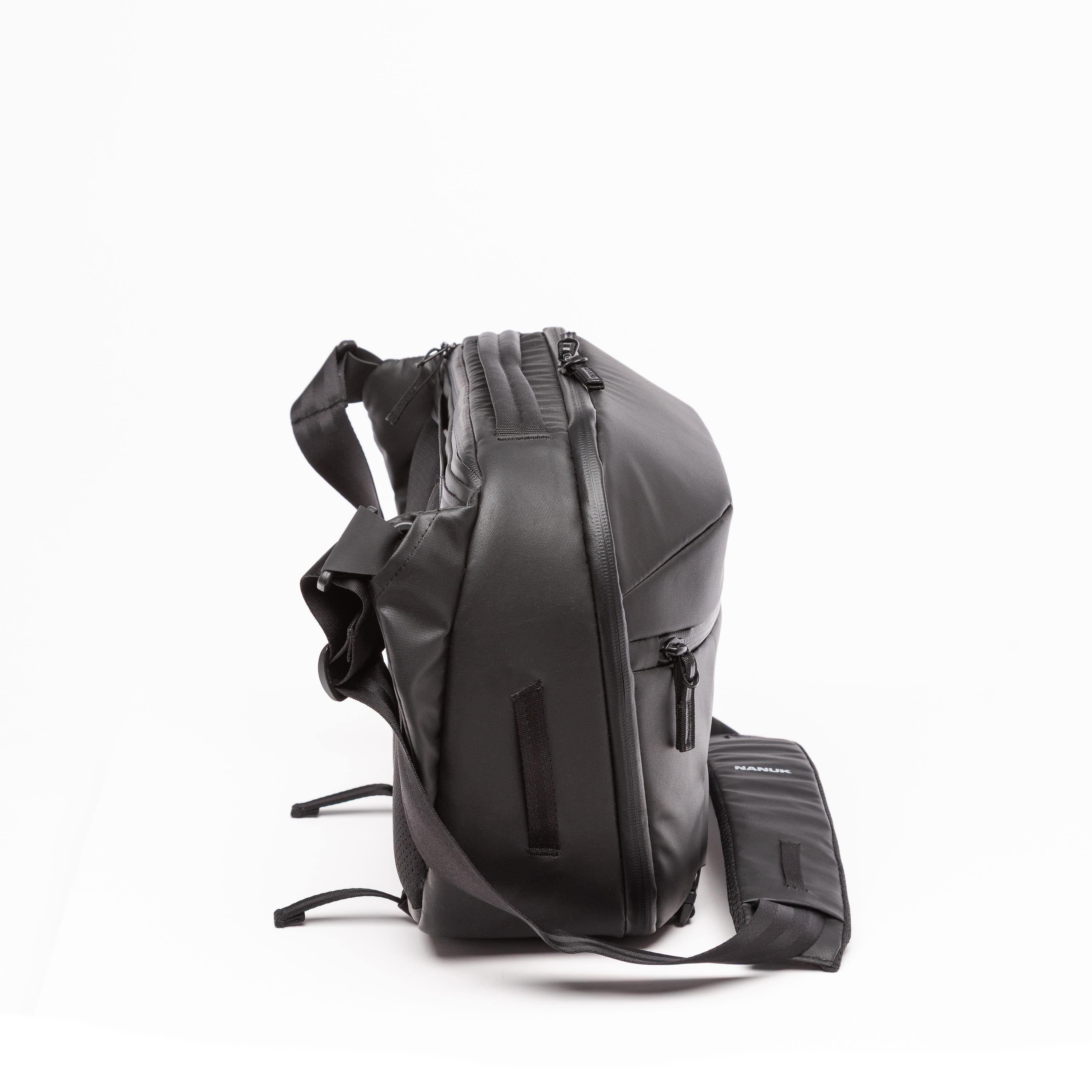 A black backpack with an attached matching pouch, shown from a side profile view on a clean white background. A black backpack with an attached matching pouch, shown from a side profile view on a clean white background.