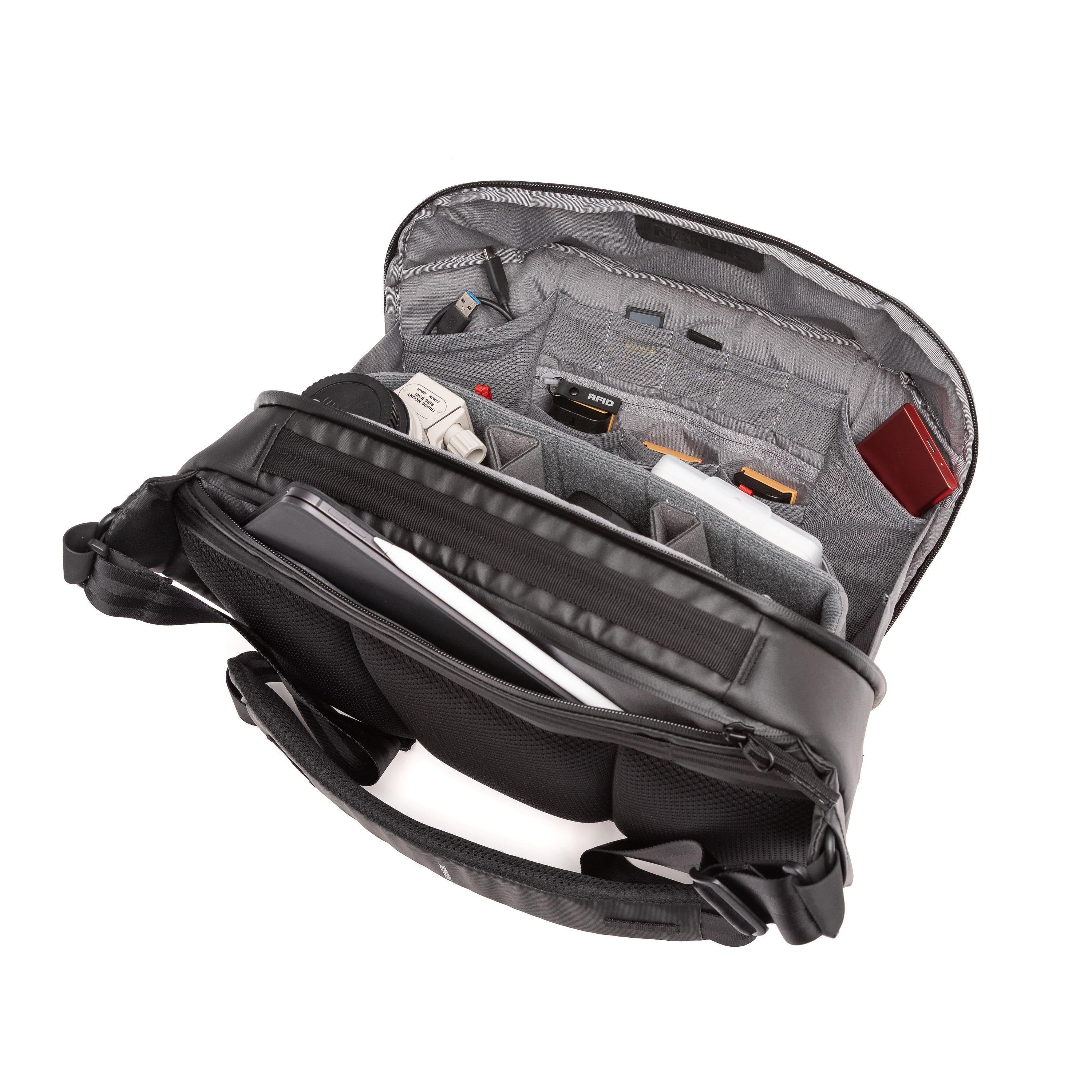 An open black and gray camera shoulder bag shown from a top-down angle, revealing multiple interior compartments, padded pockets, and storage slots filled with camera accessories. An open black and gray camera shoulder bag shown from a top-down angle, revealing multiple interior compartments, padded pockets, and storage slots filled with camera accessories.
