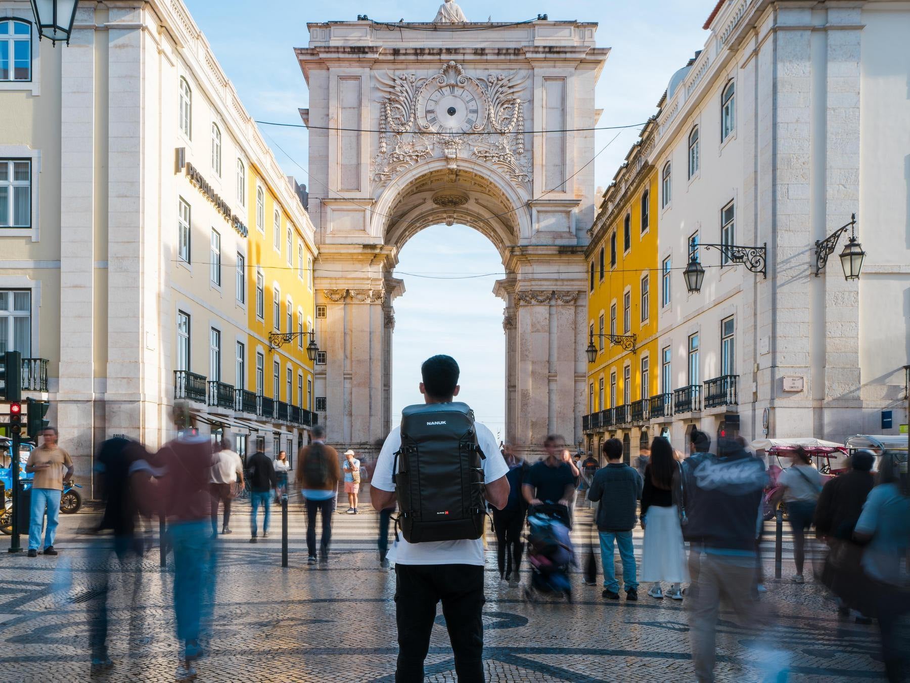 People walking in a city square with a large archway in the background