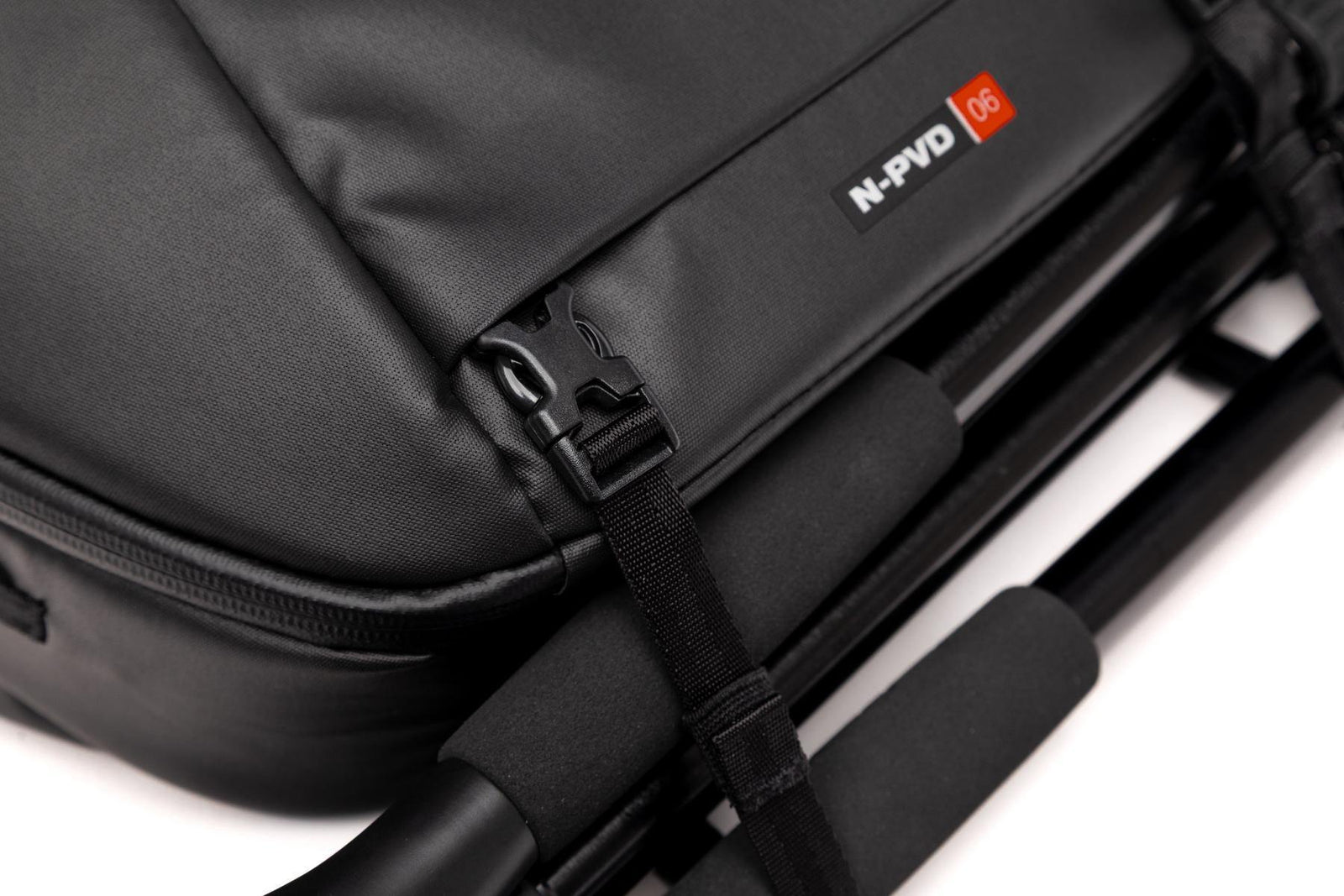 Close-up of a black N-PVD T6 camera bag with a black strap and a small red and white logo patch on a white background.