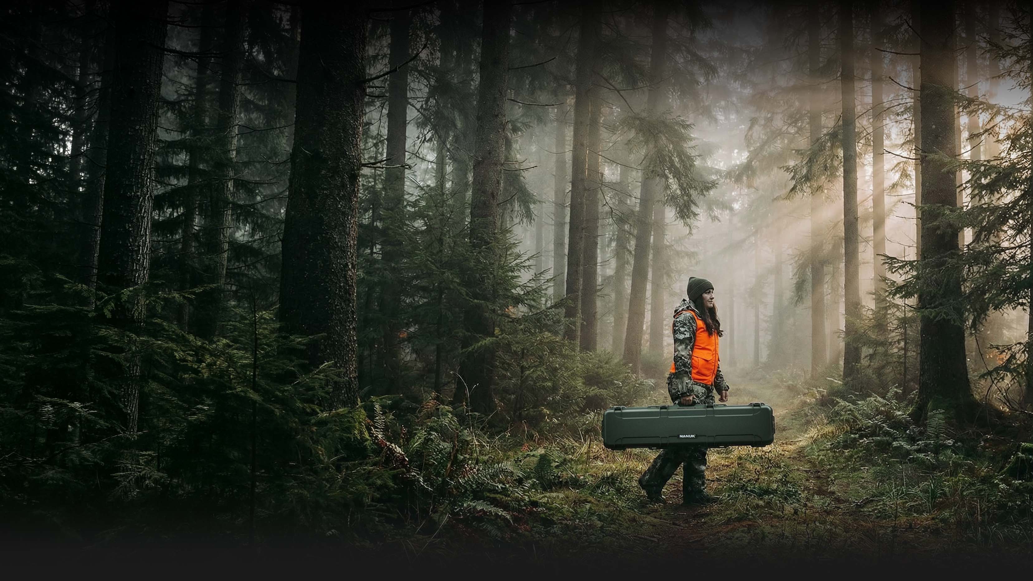 A hunter in camouflage and an orange vest carries a Nanuk case through a misty forest, highlighting nanuk cases hunting and outdoor promotion.