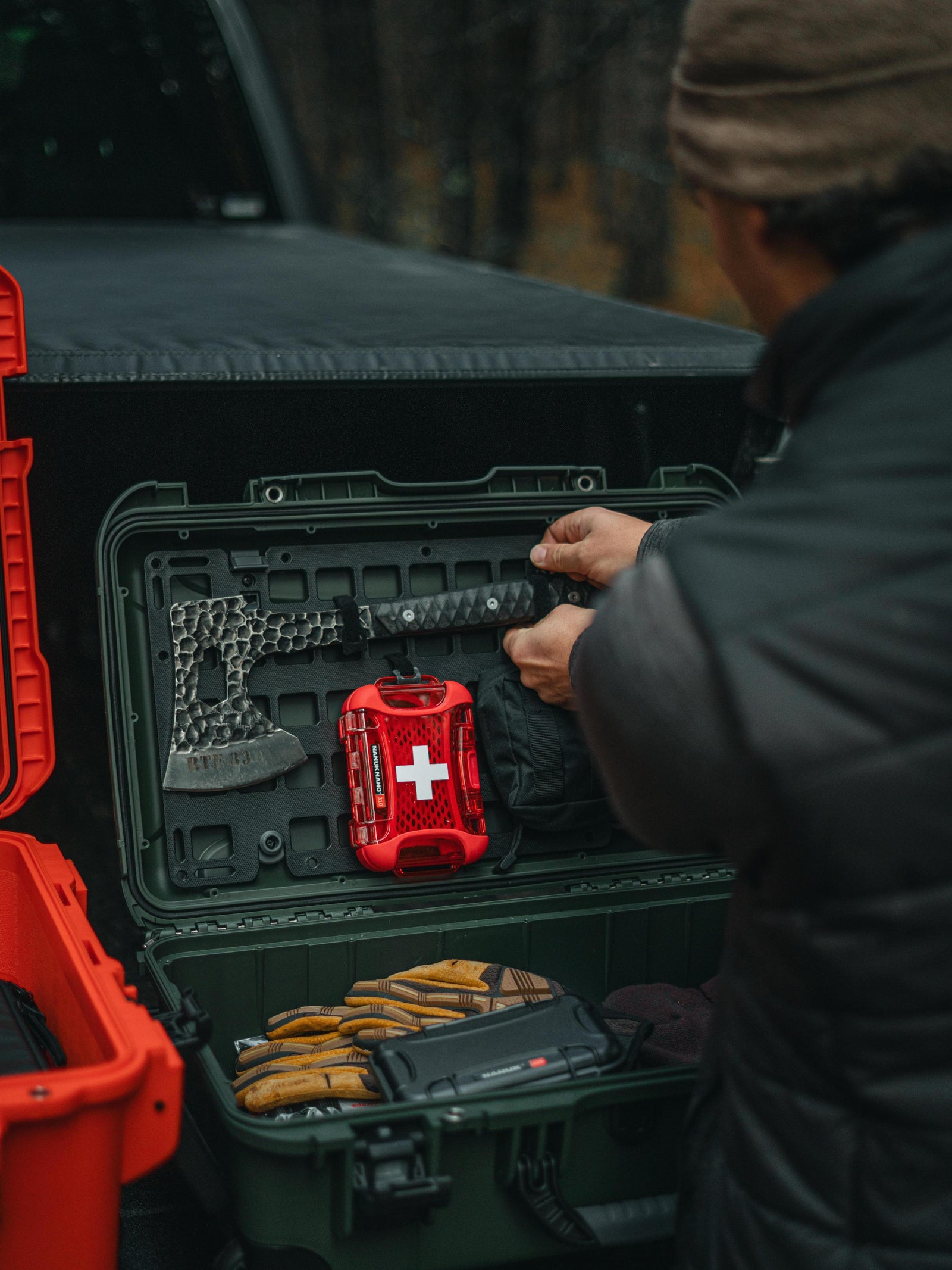 Person opening a green tool box with a red first aid kit inside, next to a black truck.