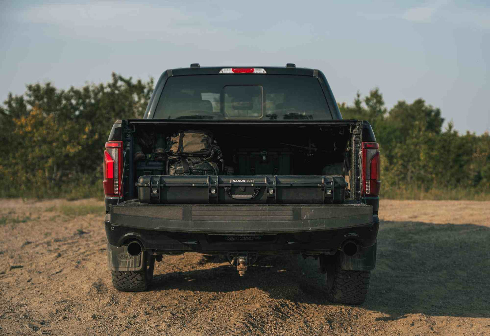 Back view of a black pickup truck with an open bed on a dirt road.