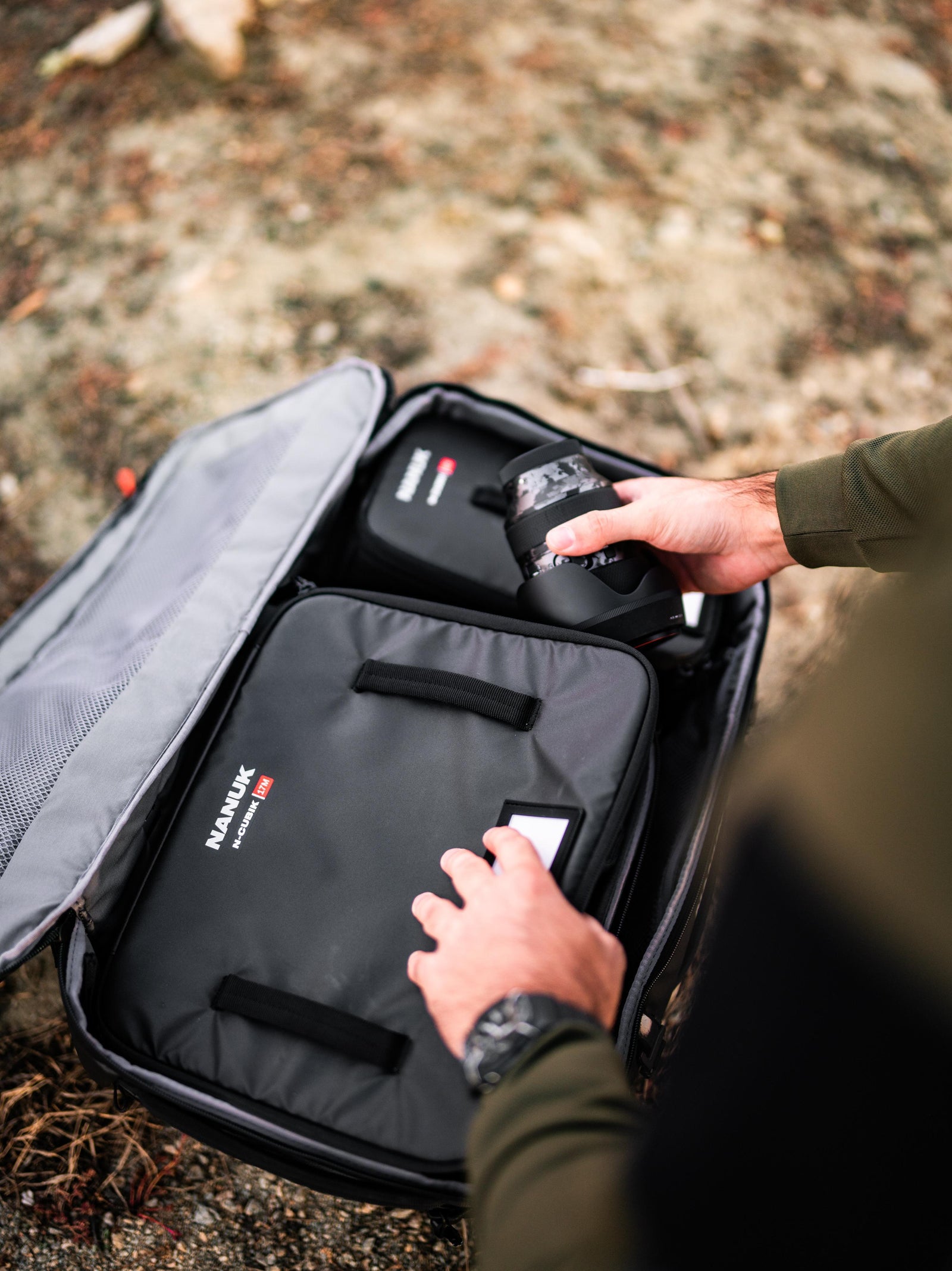 Person opening a gray suitcase with 'NANUK' branding outdoors.