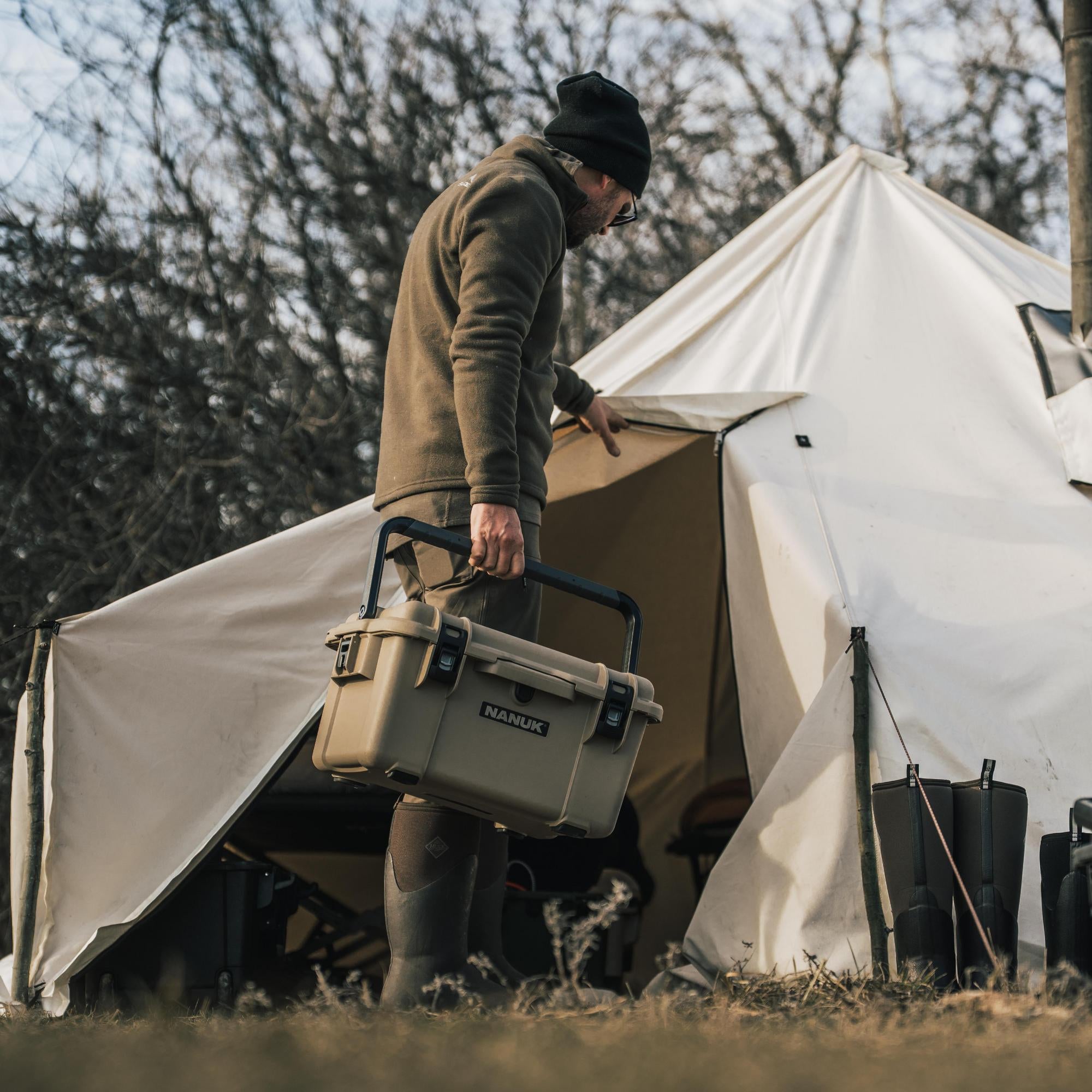Person holding a cooler near a tent in a camping setting