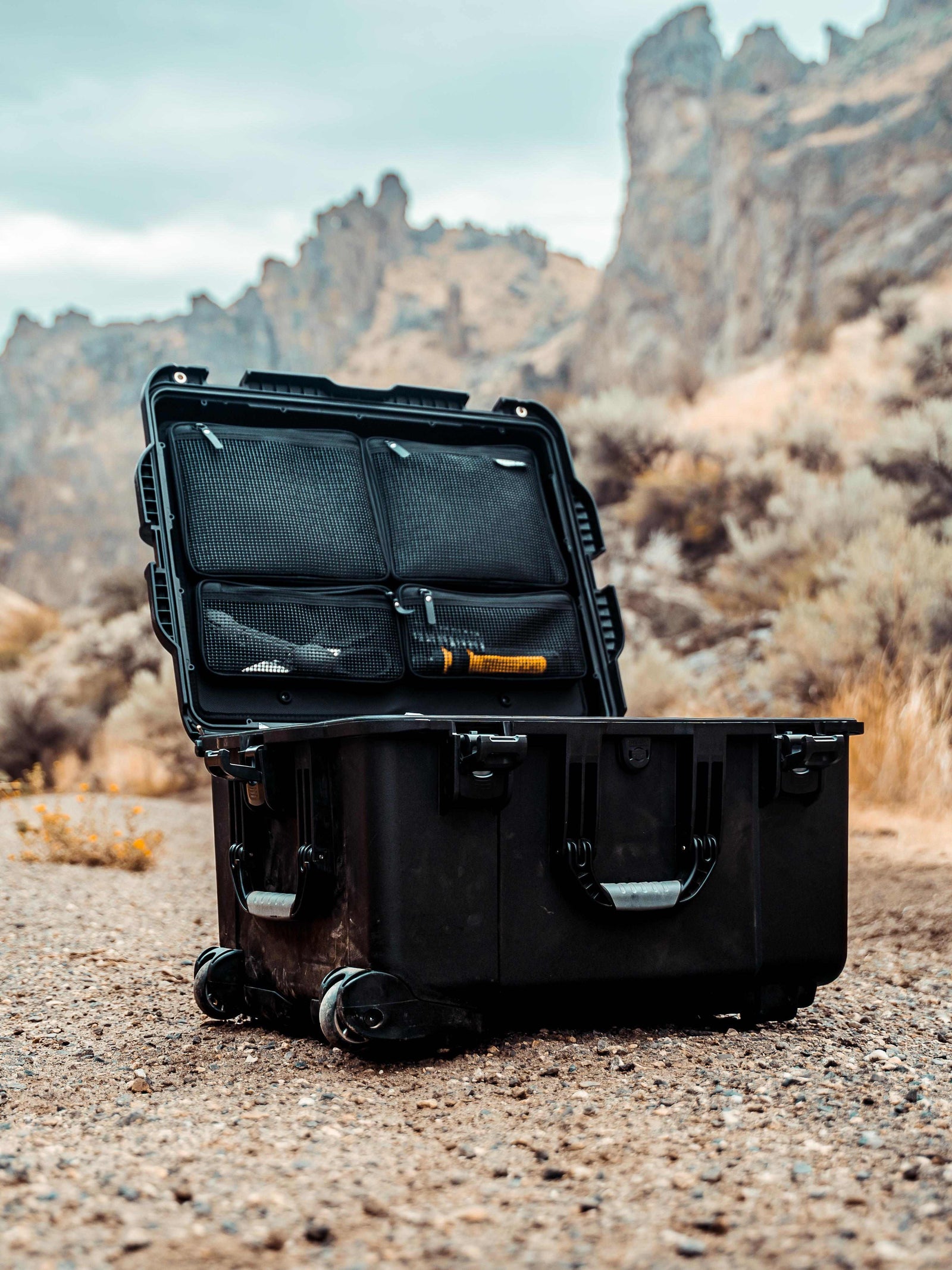 Black open suitcase with contents on a rocky desert landscape