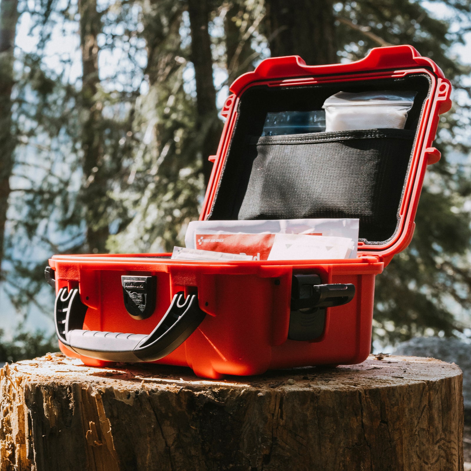 Red NANUK First Aid Kit displayed open on a tree stump in the forest, showcasing interior compartments.