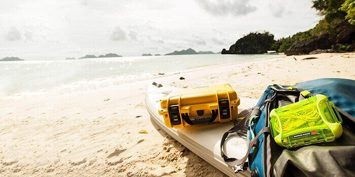 Nanuk orange case and Nano lime case outdoor on the beach with a paddleboard