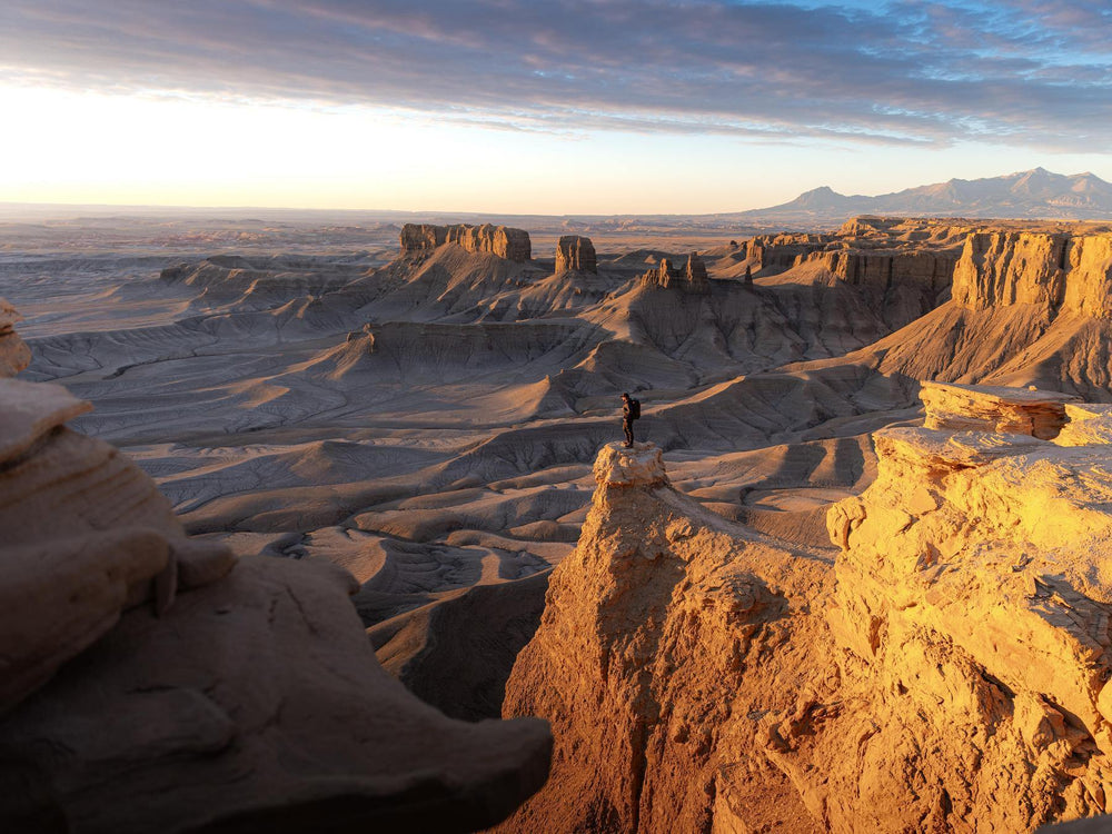 Person standing on a rocky outcrop in a desert landscape with mountains in the distance.