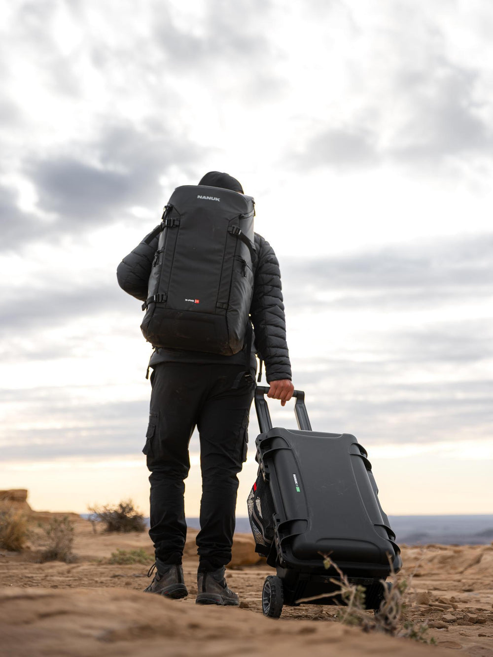 Person with a large backpack and suitcase walking in a desert landscape