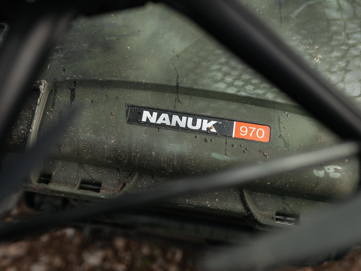 Close-up of a dark green Nanuk 970 machine body with a black and orange brand sticker, partially framed by blurred black bars in the foreground.
