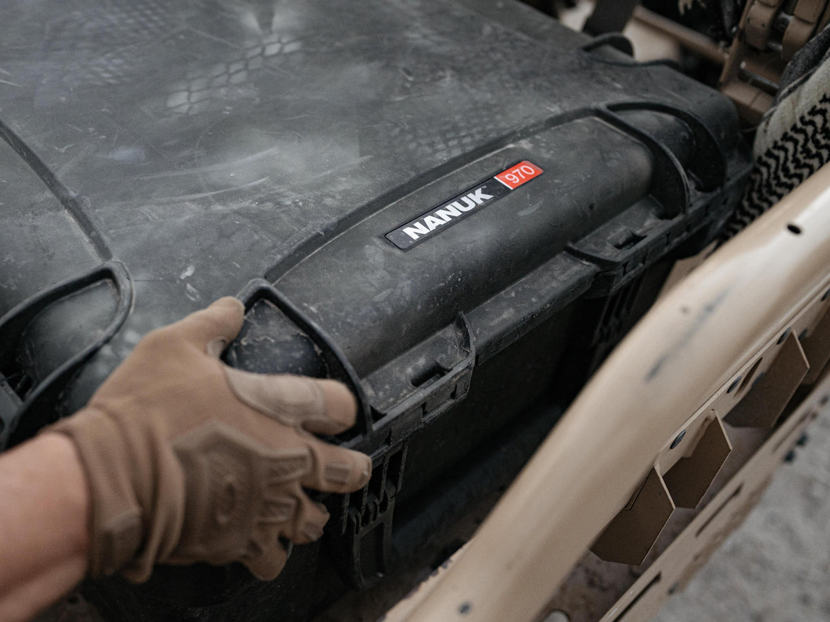 A close-up shot of a person's gloved hand opening a heavy-duty black Nanuk D10 storage case mounted on a vehicle. The case features a prominent black label with the white 'NANUK' brand name and a red 'D10' size badge.