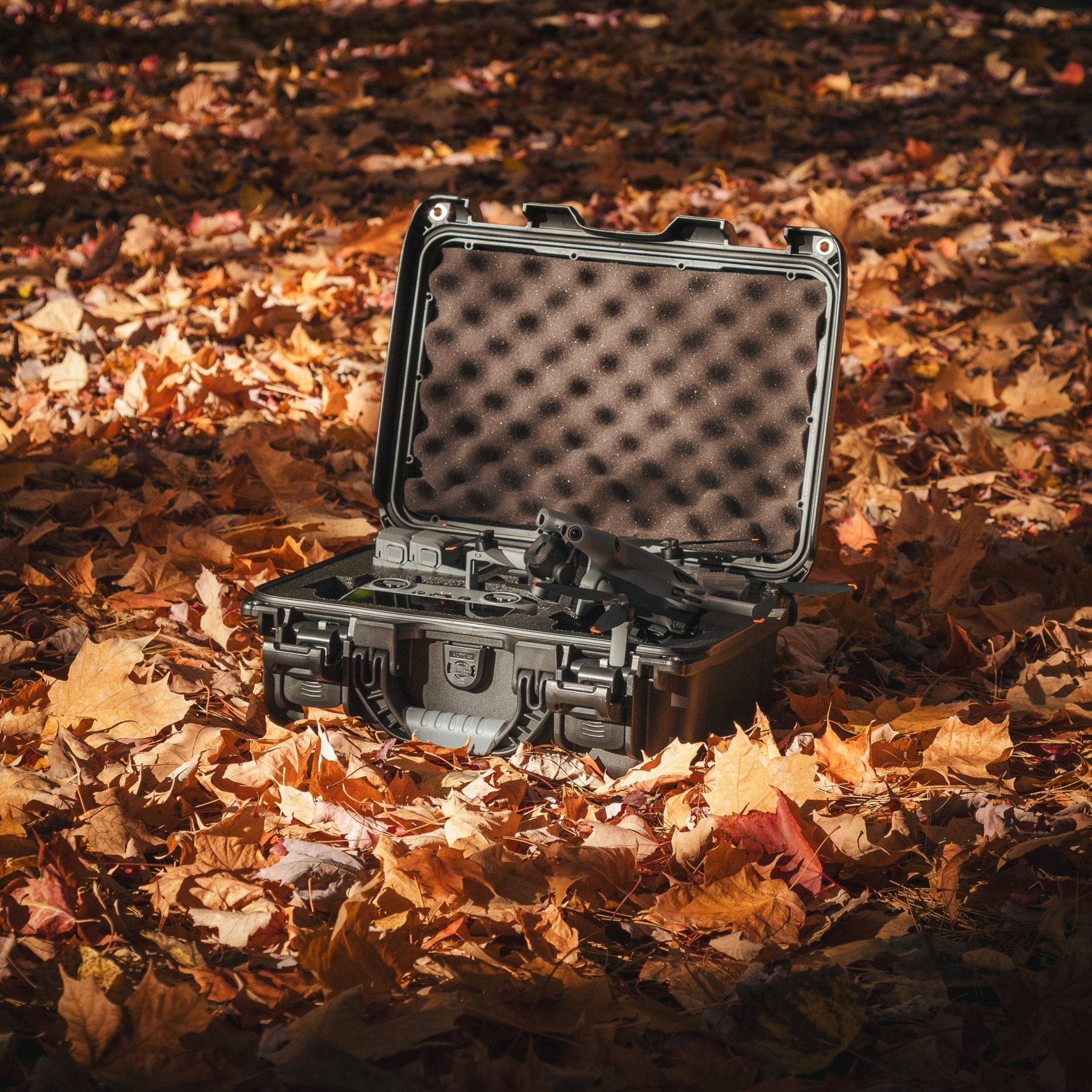 Black hard-shell case with foam interior on a bed of autumn leaves