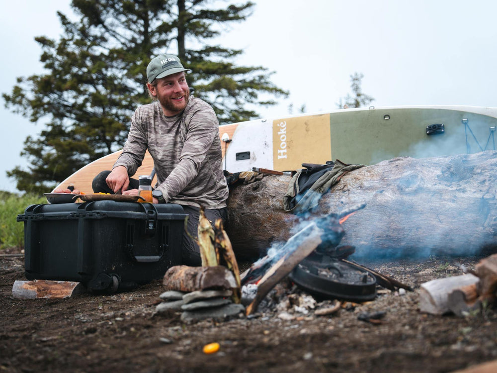 Man cooking over a campfire with a portable stove and equipment in a forest setting