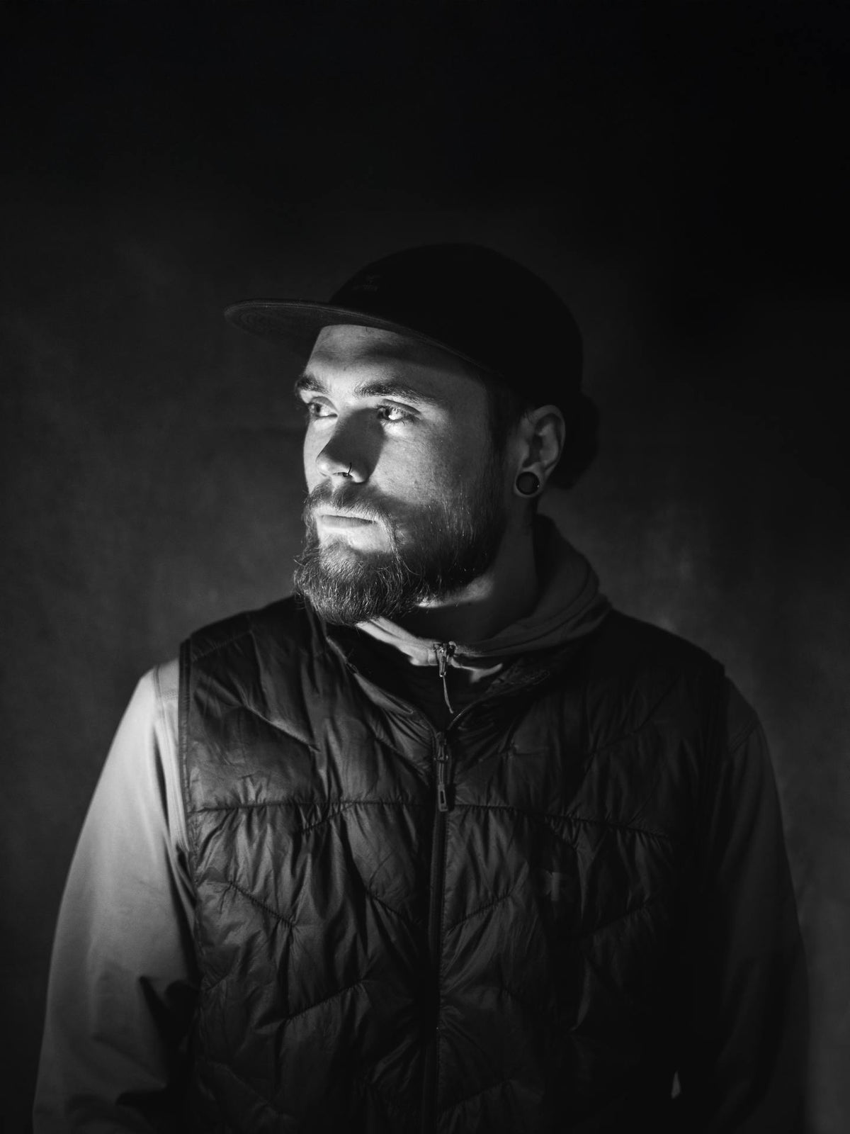 Man wearing a cap and puffer vest against a dark background