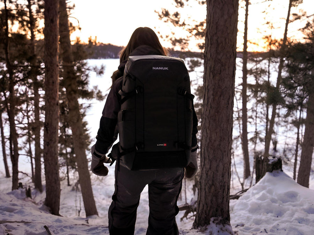 Person with a black backpack walking through a snowy forest