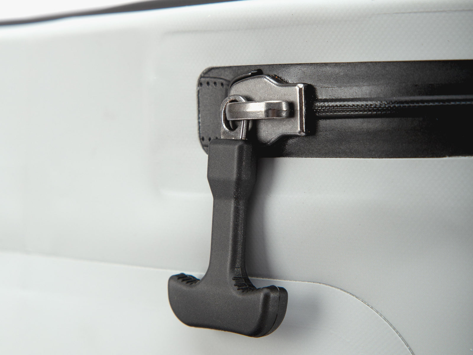 Close-up of a black zipper pull tab with a silver metal slider on a white surface.