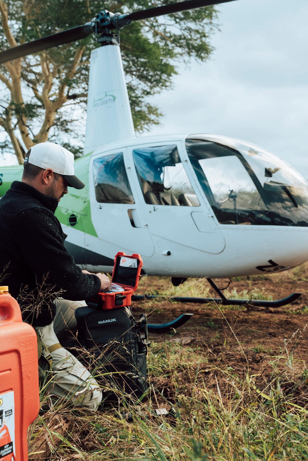 Person with a toolbox near a helicopter in a natural setting