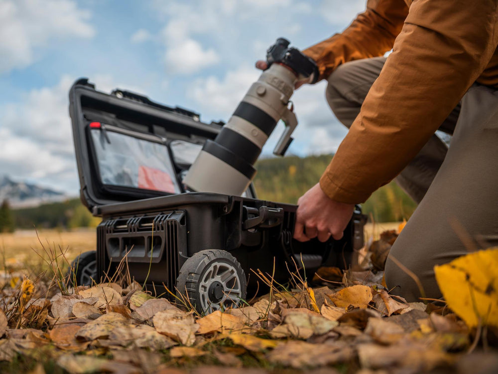 Person setting up a camera with a large lens on a tripod outdoors.