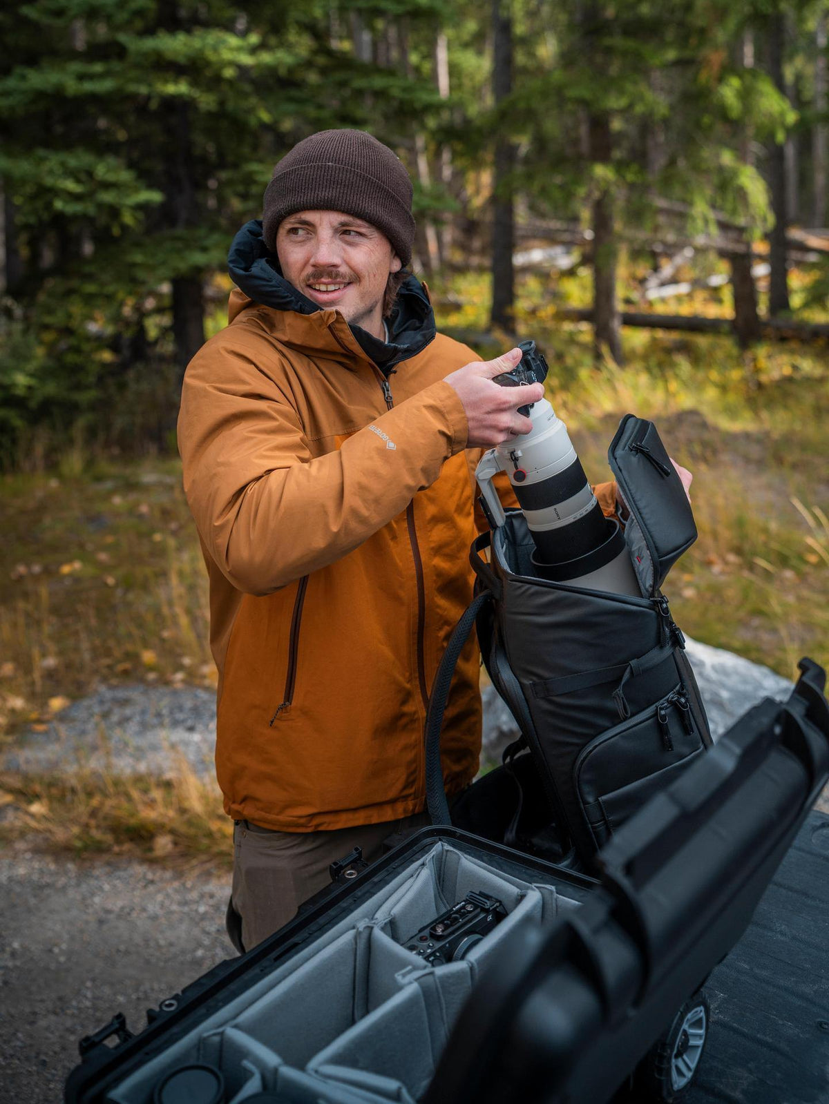 Man holding a large camera lens in a forest setting
