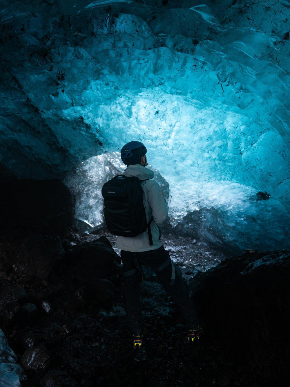 Person exploring an ice cave with a backpack, illuminated by the blue glow of the ice.