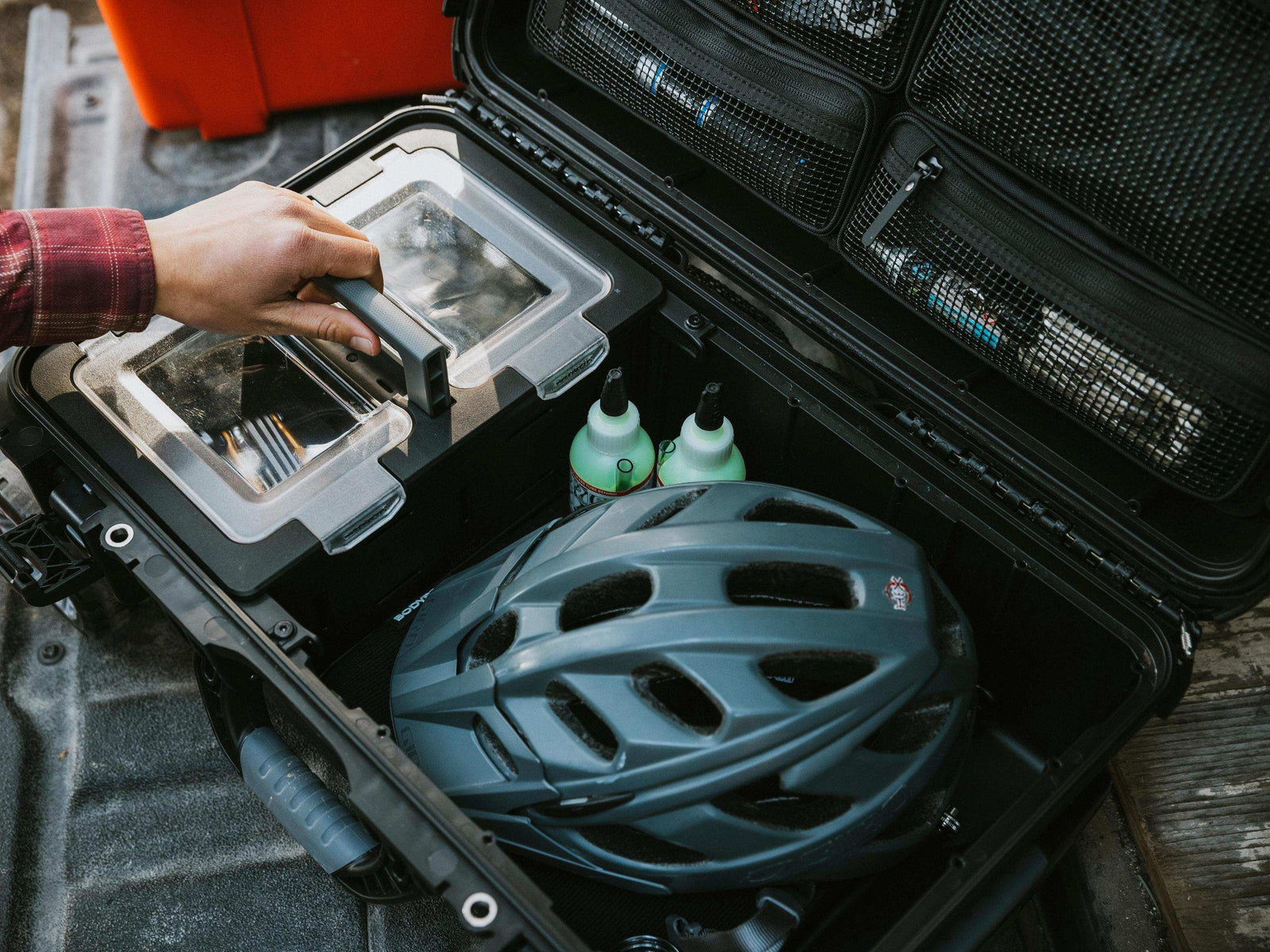 Helmet inside an open black hard-shell travel case with a person's hand reaching in.
