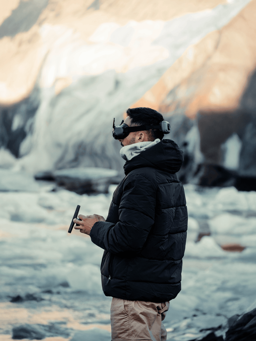 Person wearing a black jacket and goggles, standing in a snowy landscape with mountains in the background.