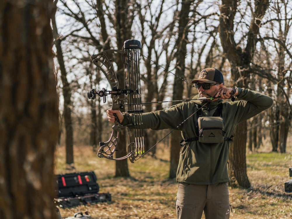 Man in camouflage gear holding a compound bow in a forest setting