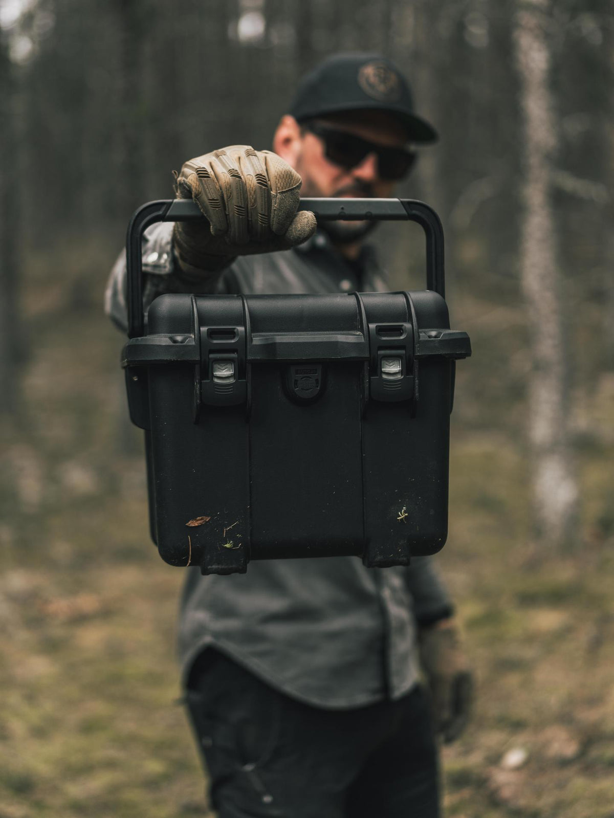Person holding a black toolbox in a forest setting