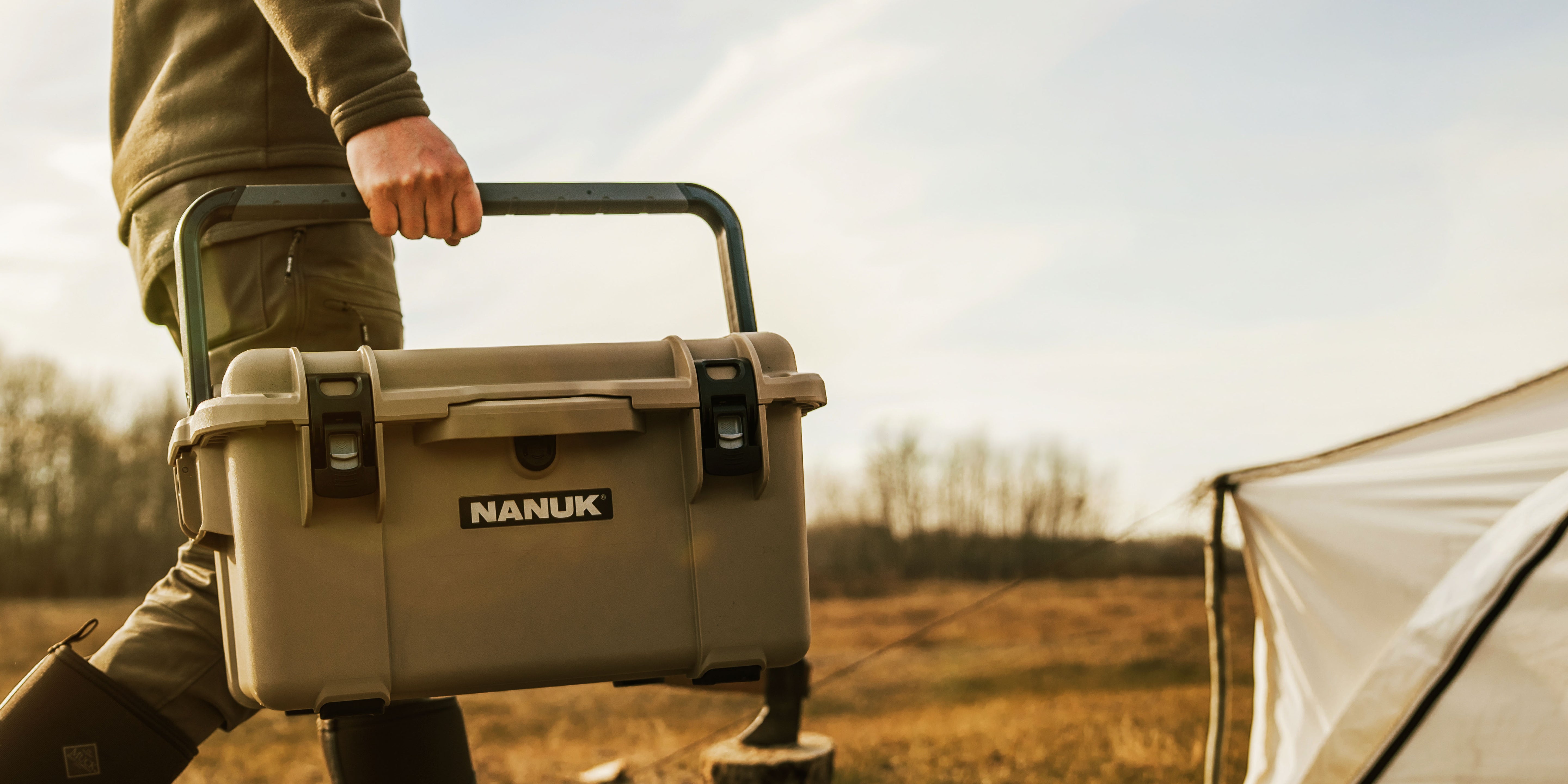 Person holding a NANUK cooler outdoors with a tent in the background
