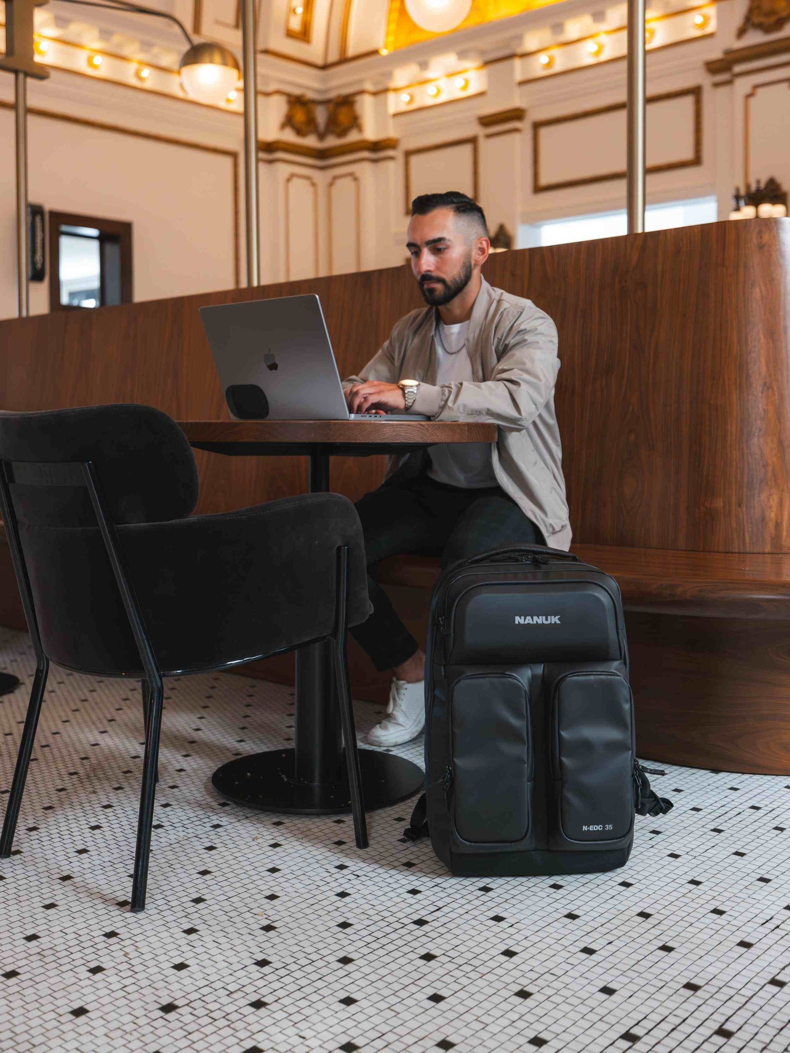 Man using a laptop with a backpack next to him in a modern cafe setting
