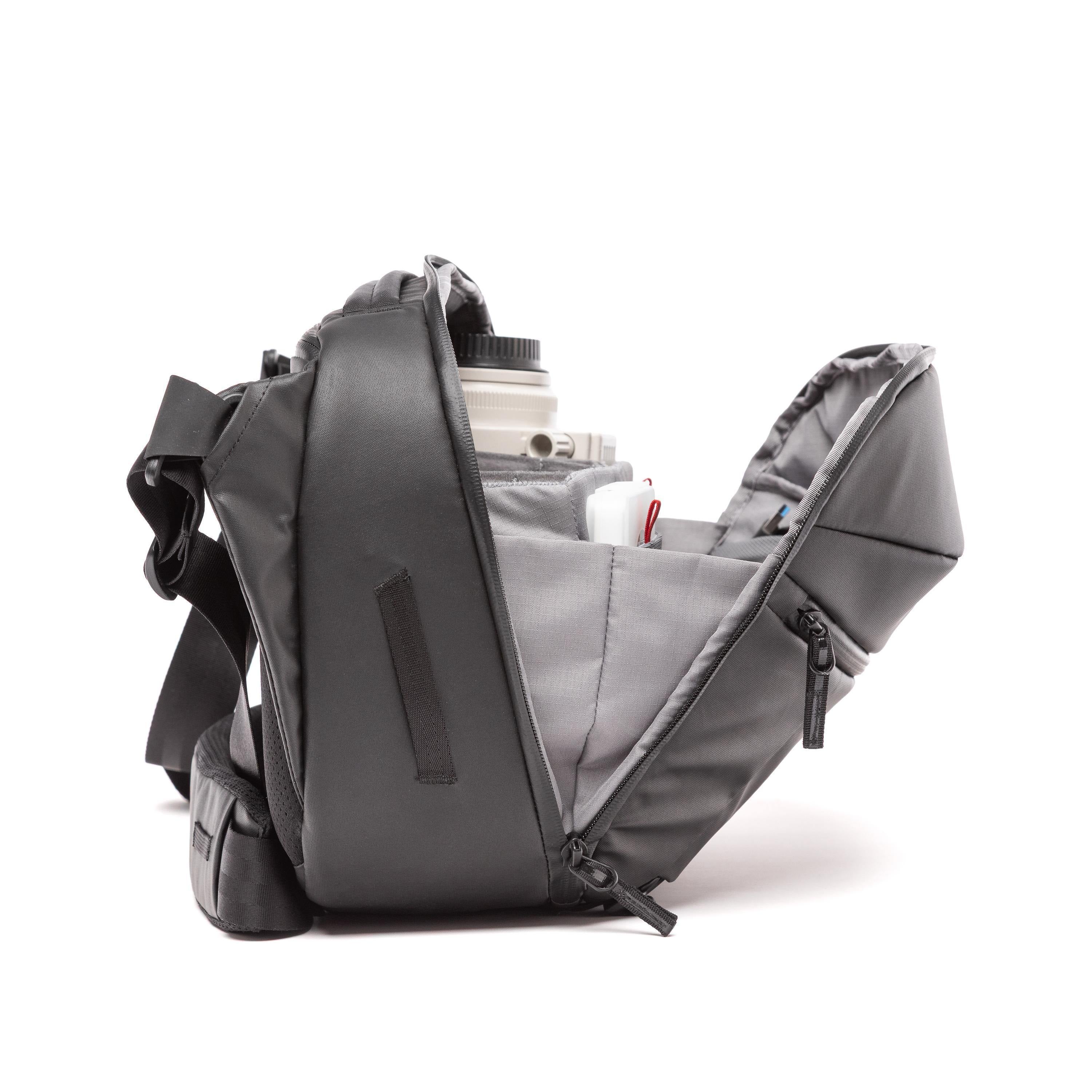 A dark gray camera shoulder bag shown open, displaying its interior compartments and a camera lens inside, set against a plain white background.