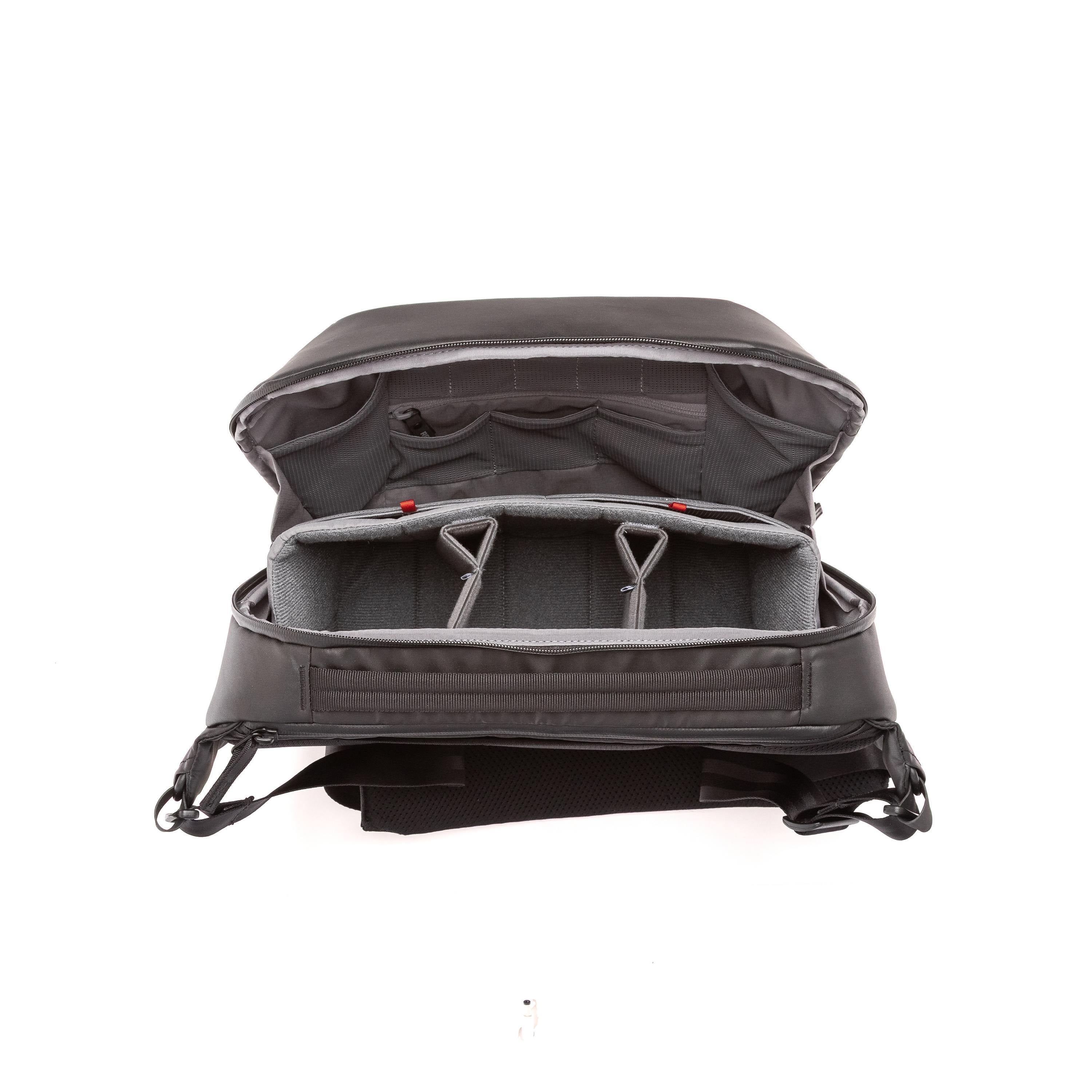 An open black camera backpack shown from the front, displaying its padded interior compartments, foam inserts, and adjustable shoulder straps against a white background.
