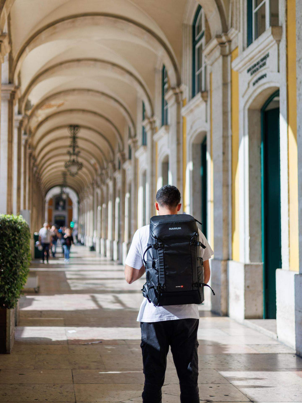 Person with a backpack walking through an archway in a sunlit hallway