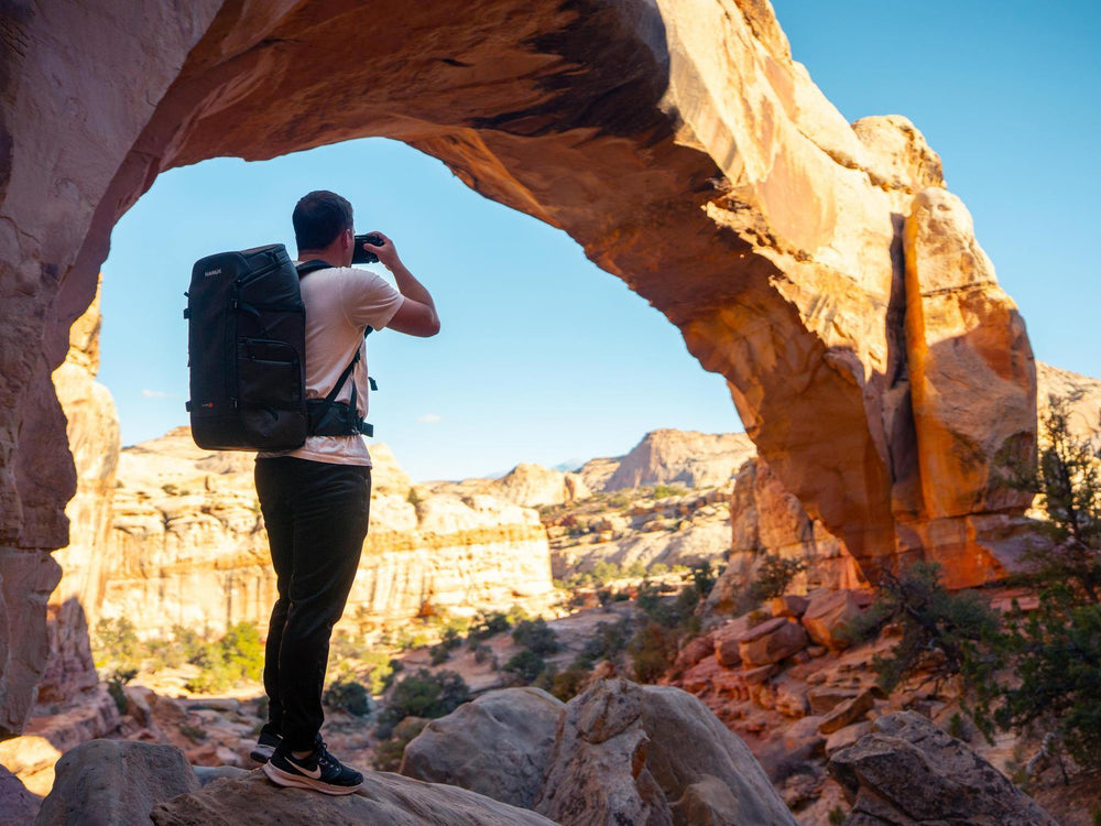 Person taking a photo of a natural rock arch with a backpack