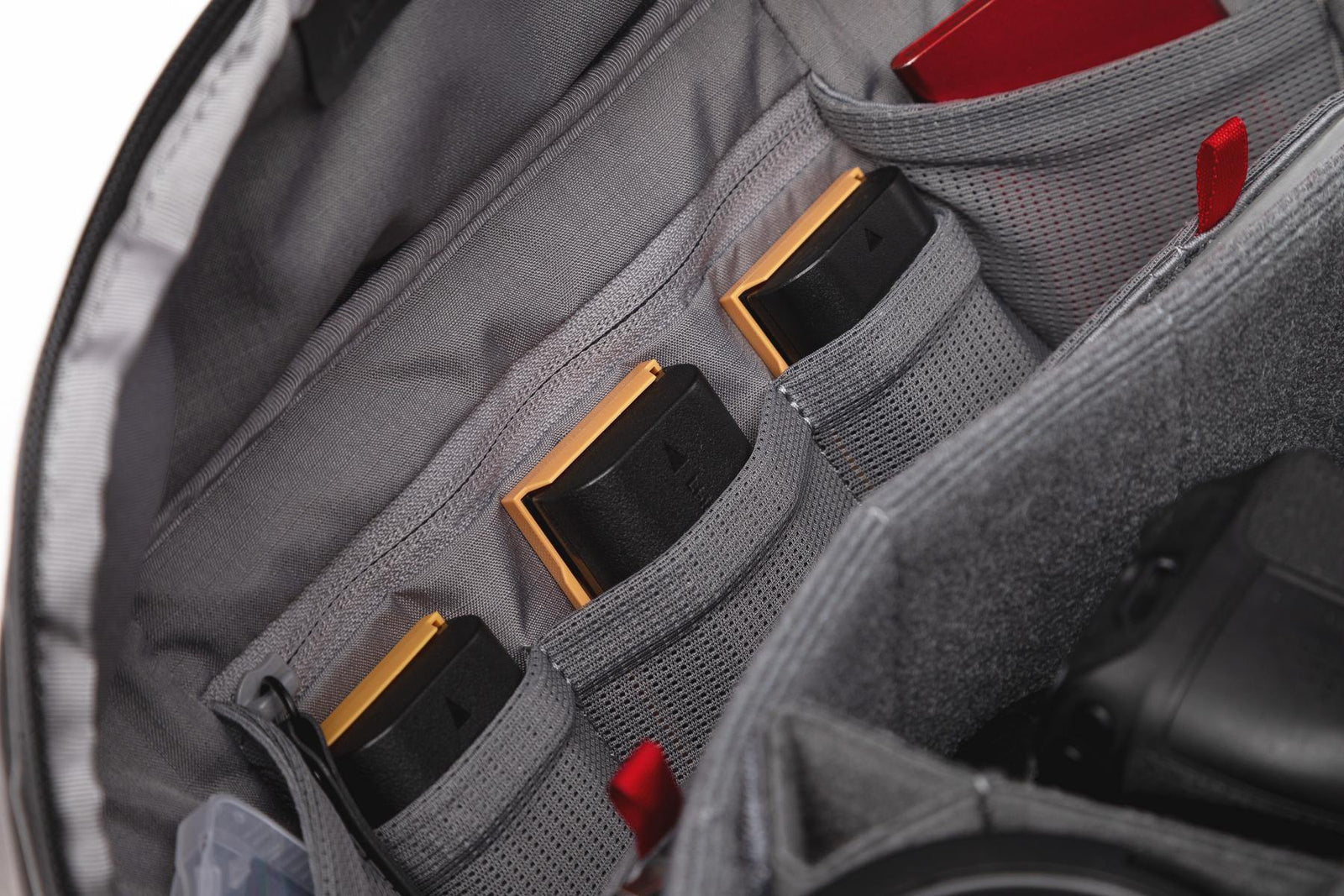 Close-up of a gray camera bag organizer with multiple mesh pockets holding black and gold camera batteries or similar rectangular accessories.
