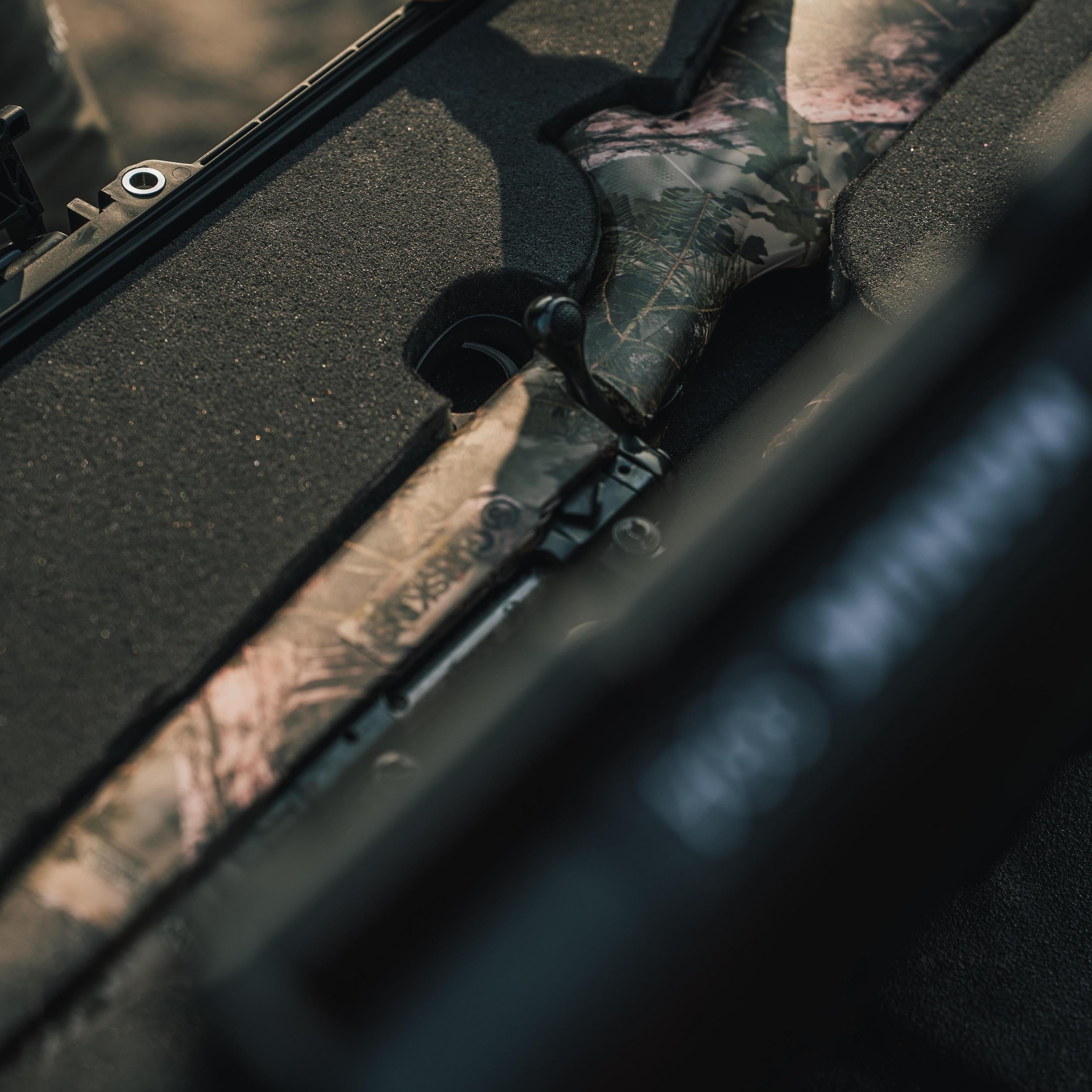 Camouflage-patterned rifle inside a vehicle with a focus on the gun grip.