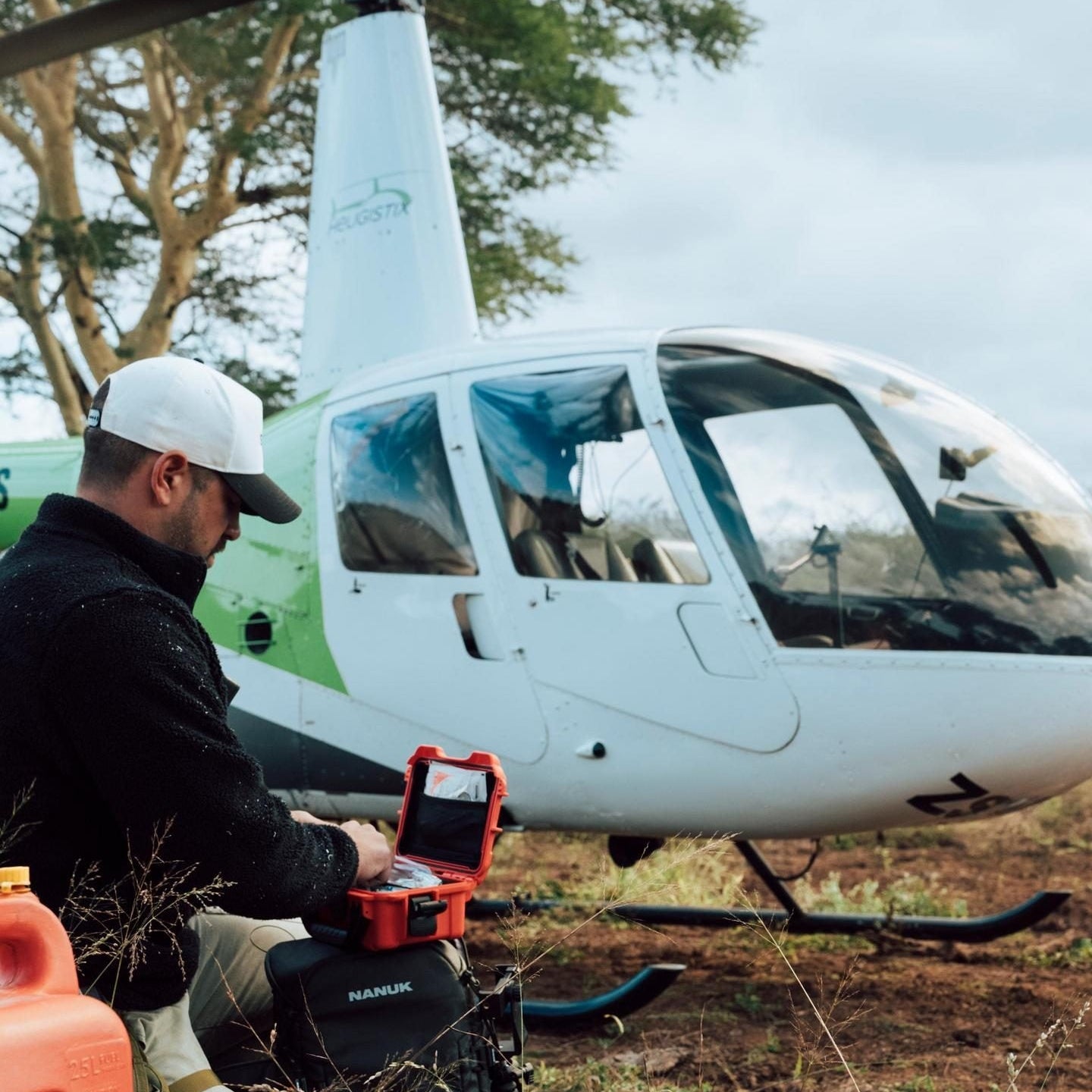 Person with a toolbox near a helicopter in a natural setting