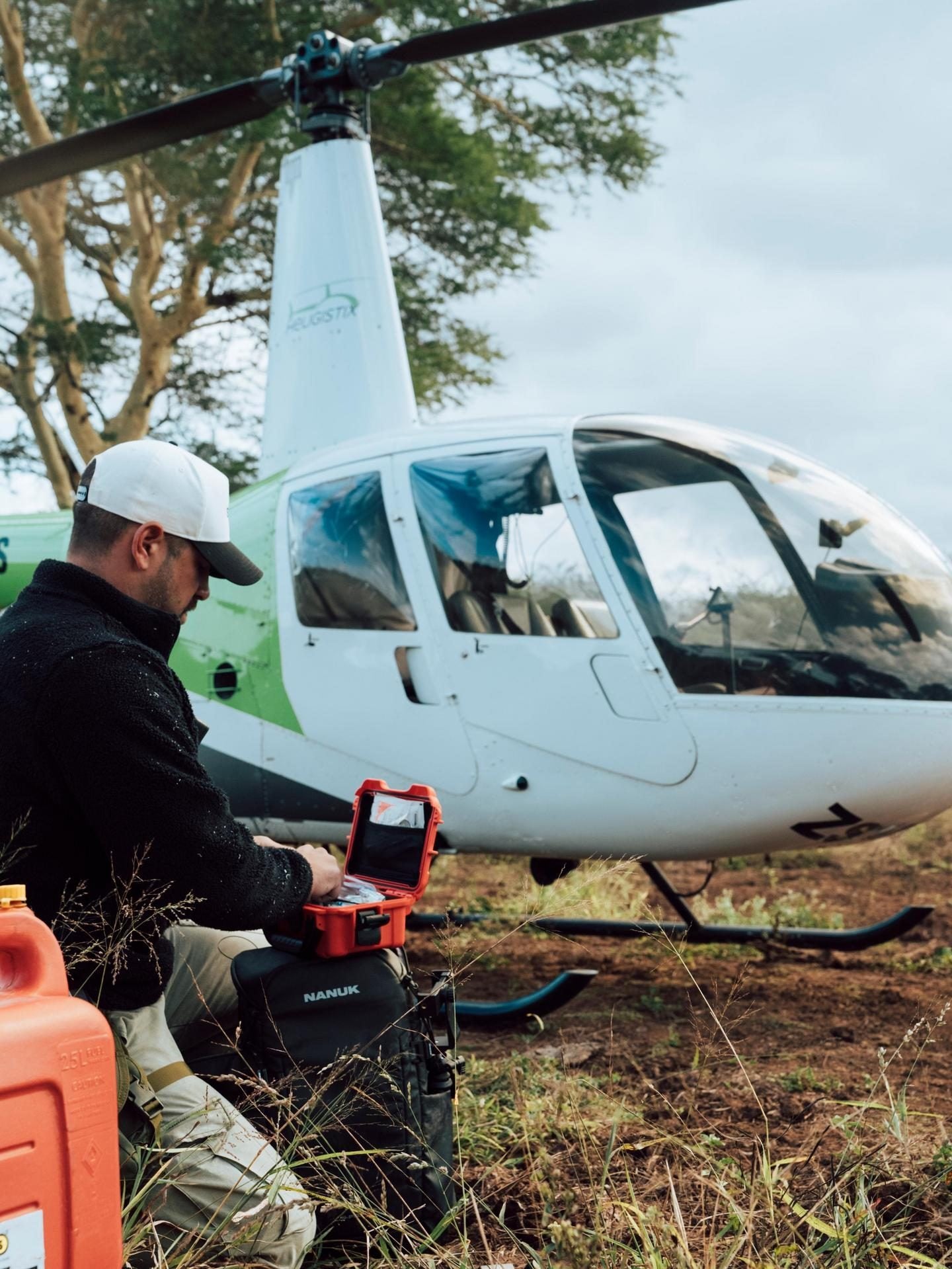 Person with a toolbox near a helicopter in a natural setting