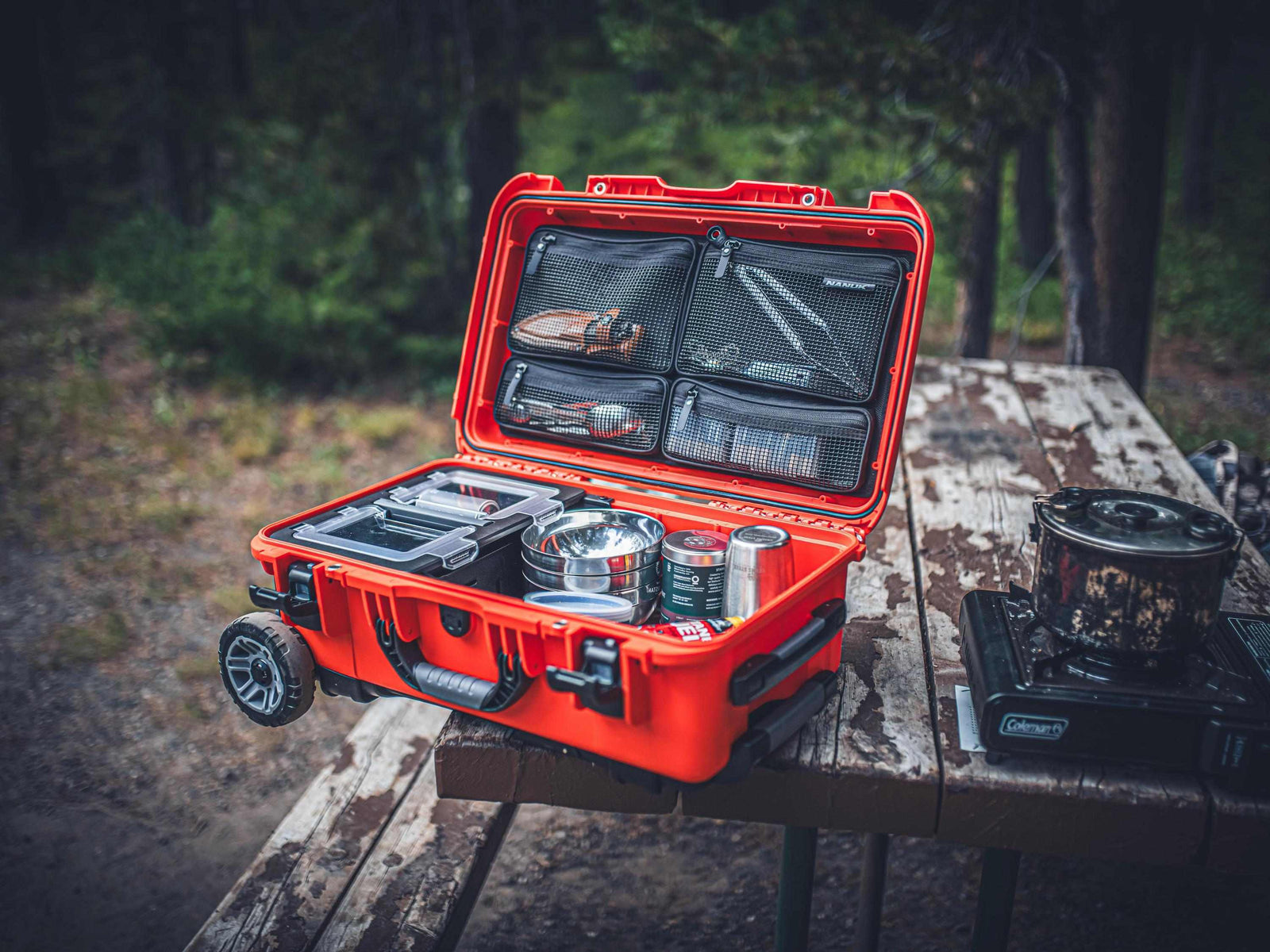 Open red tool case on a wooden table with camping gear inside, outdoors.