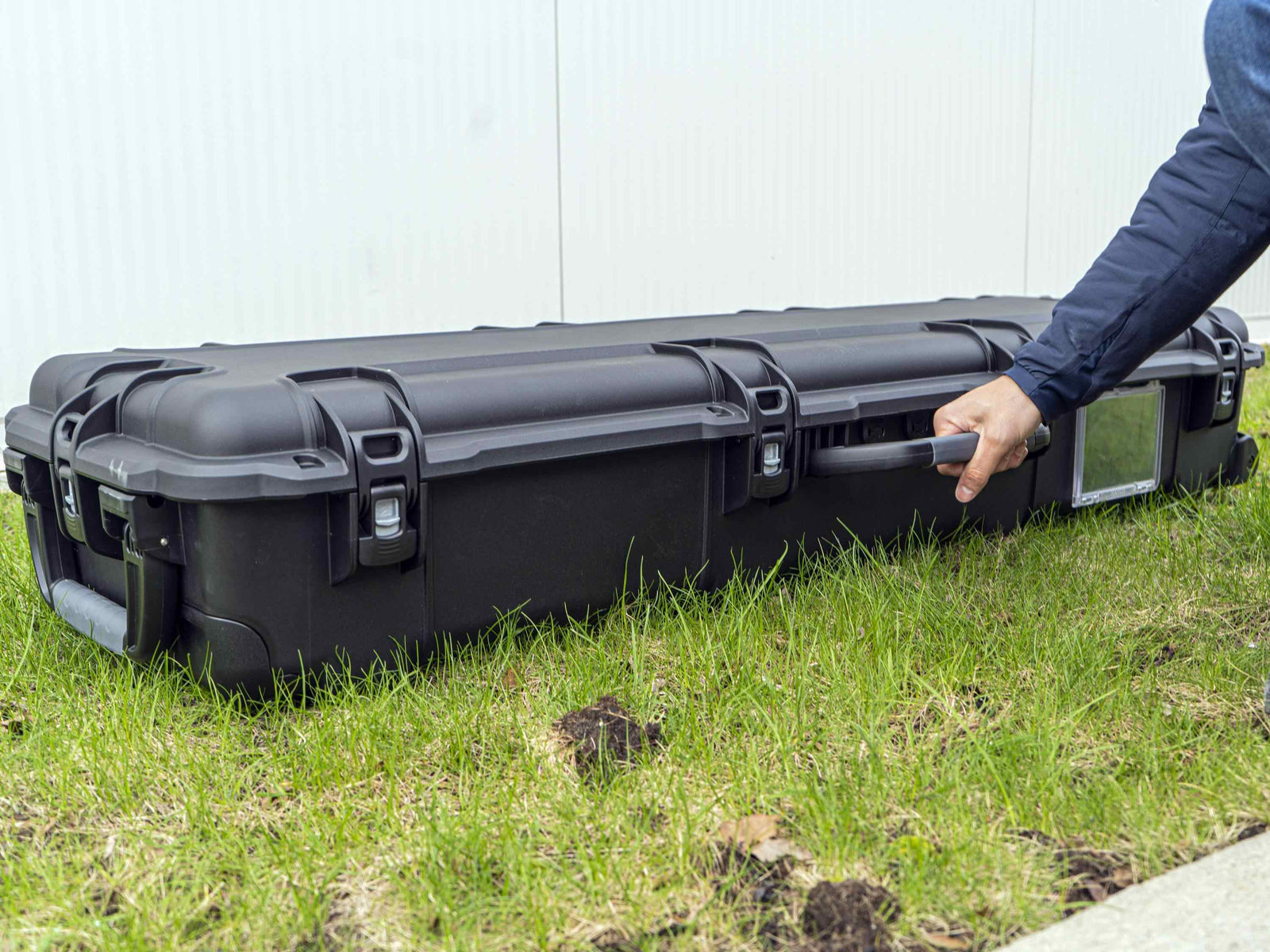 Person opening a large black hard-shell case on grass